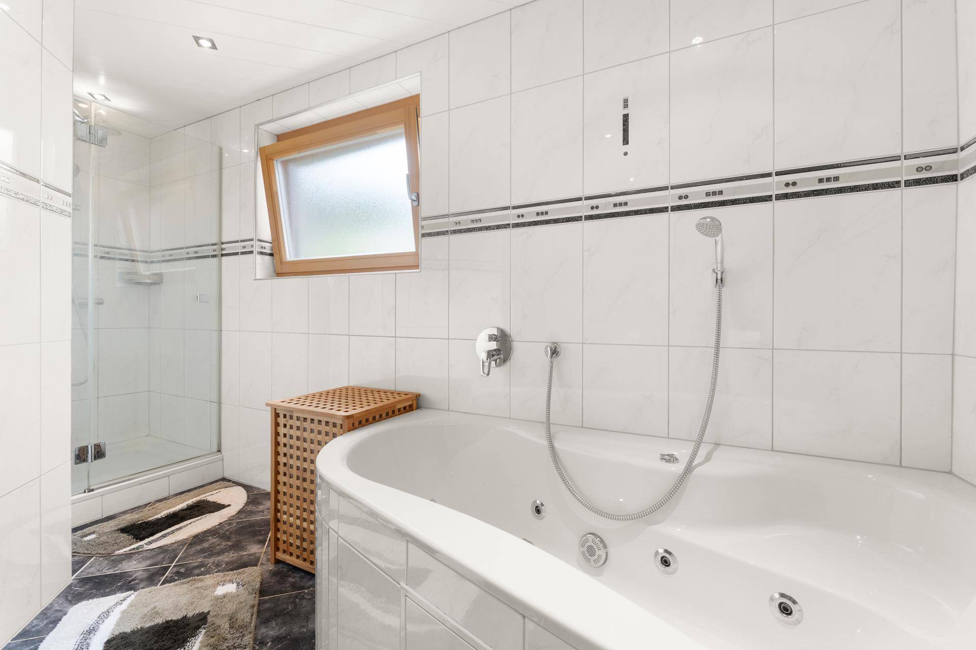 Helles Badezimmer mit Whirlpool-Badewanne, Duschkabine und Fenster.
