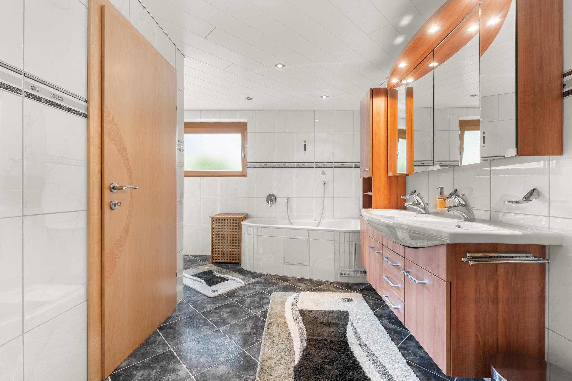 Geräumiges Badezimmer mit Doppelwaschbecken, Badewanne und modernen Fliesen.