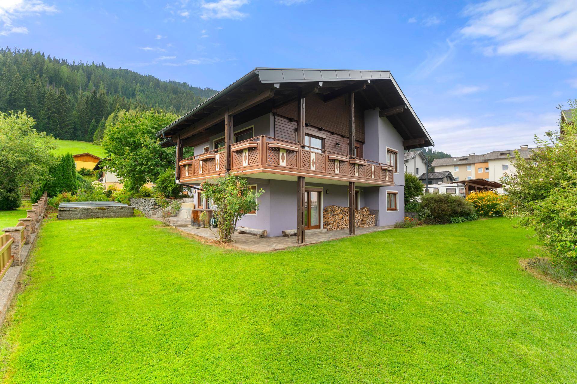 Großzügiges Haus mit Balkonen und weitläufigem Rasenbereich, umgeben von grüner Natur.