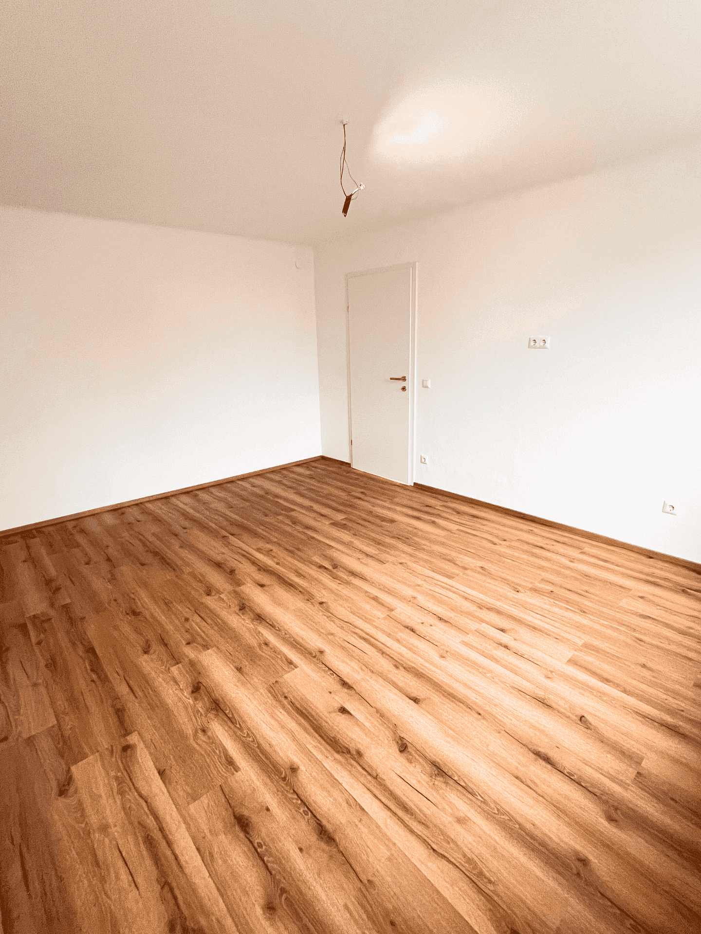 Geräumiges Zimmer mit Holzboden und weiß gestrichenen Wänden, bereit zur Einrichtung.