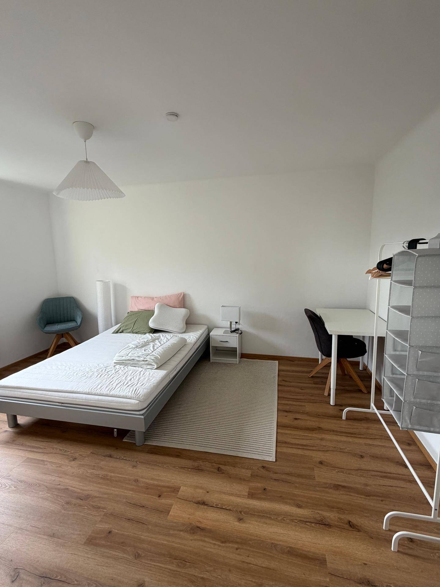 Helles Schlafzimmer mit Einzelbett, Schreibtisch und Holzboden, modern eingerichtet.