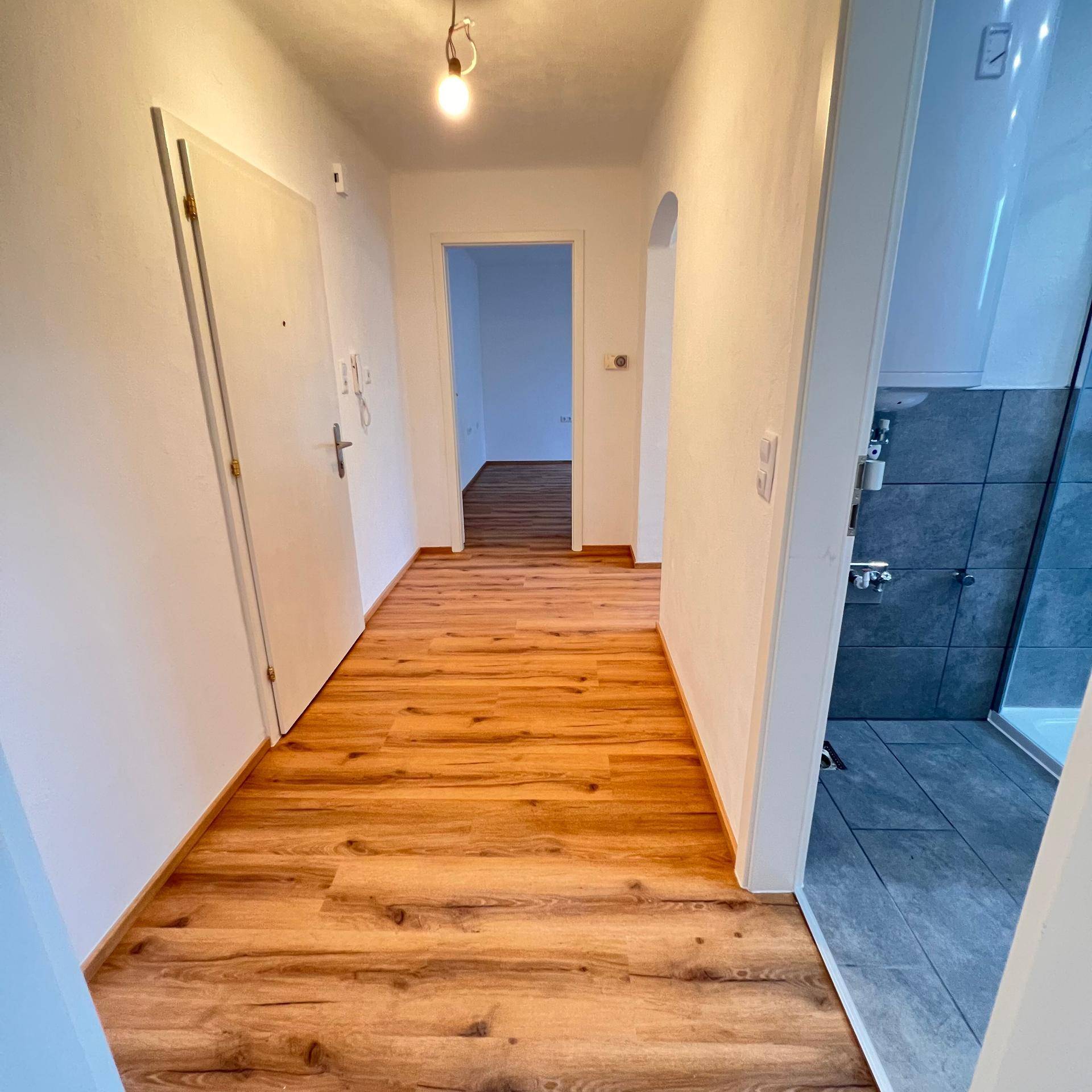 Heller Flur mit Holzboden, der zu den verschiedenen Räumen der Wohnung führt.