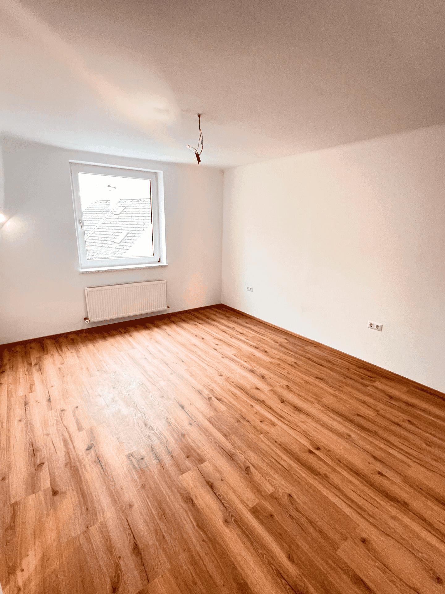 Helles, leeres Zimmer mit Holzboden und Fenster, ideal als Schlafzimmer oder Arbeitszimmer.