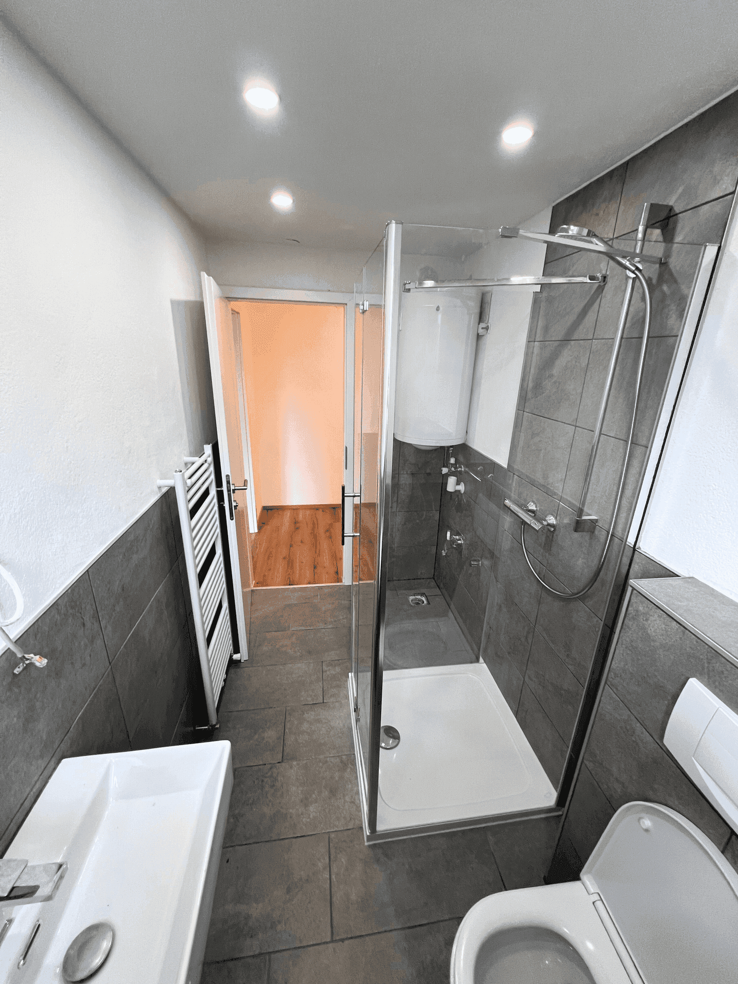 Modernes Badezimmer mit grauen Fliesen, Duschkabine, Waschbecken und beheiztem Handtuchhalter.