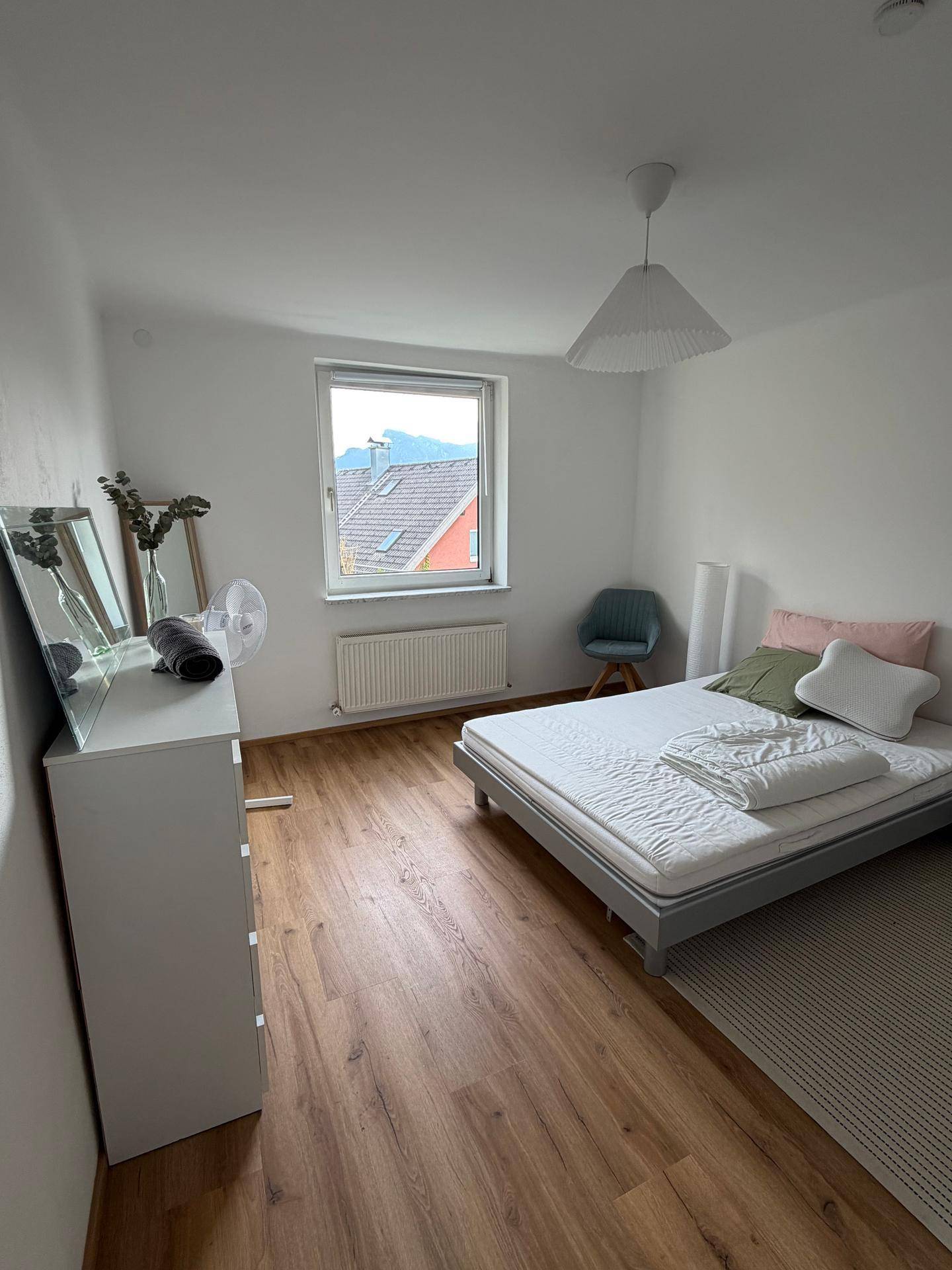 Schlafzimmer mit Einzelbett, Kommode und Fensterblick auf die umliegende Landschaft und Berge.