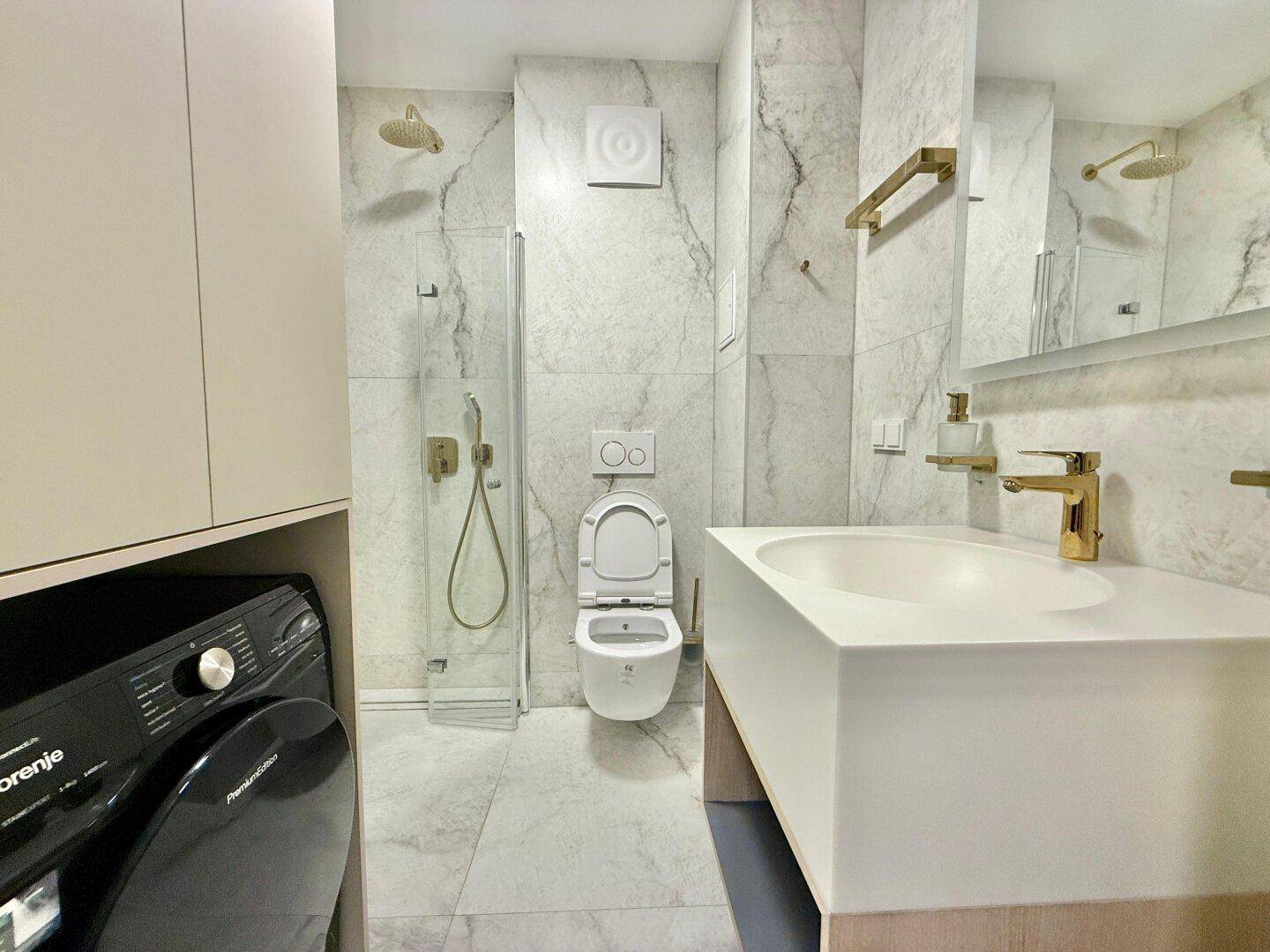 Modernes Badezimmer mit Marmorfliesen, Dusche und integrierter Waschmaschine.