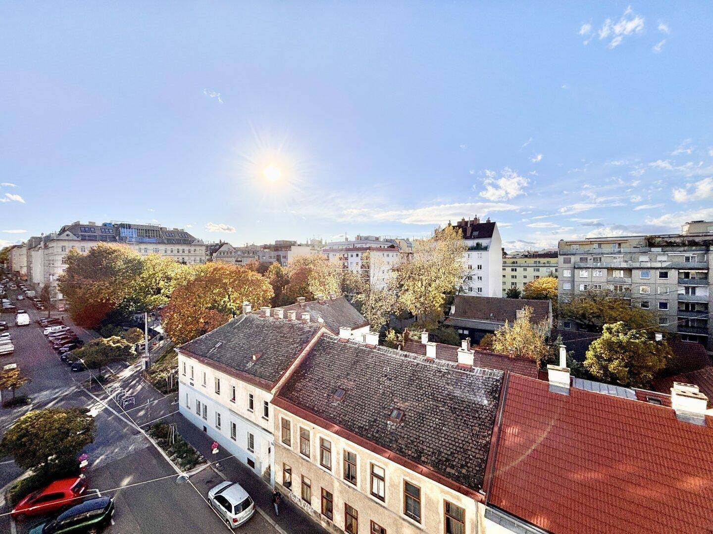 Sonnige Ansicht einer Wohnstraße mit herbstlichen Bäumen und Gebäuden unter blauem Himmel.