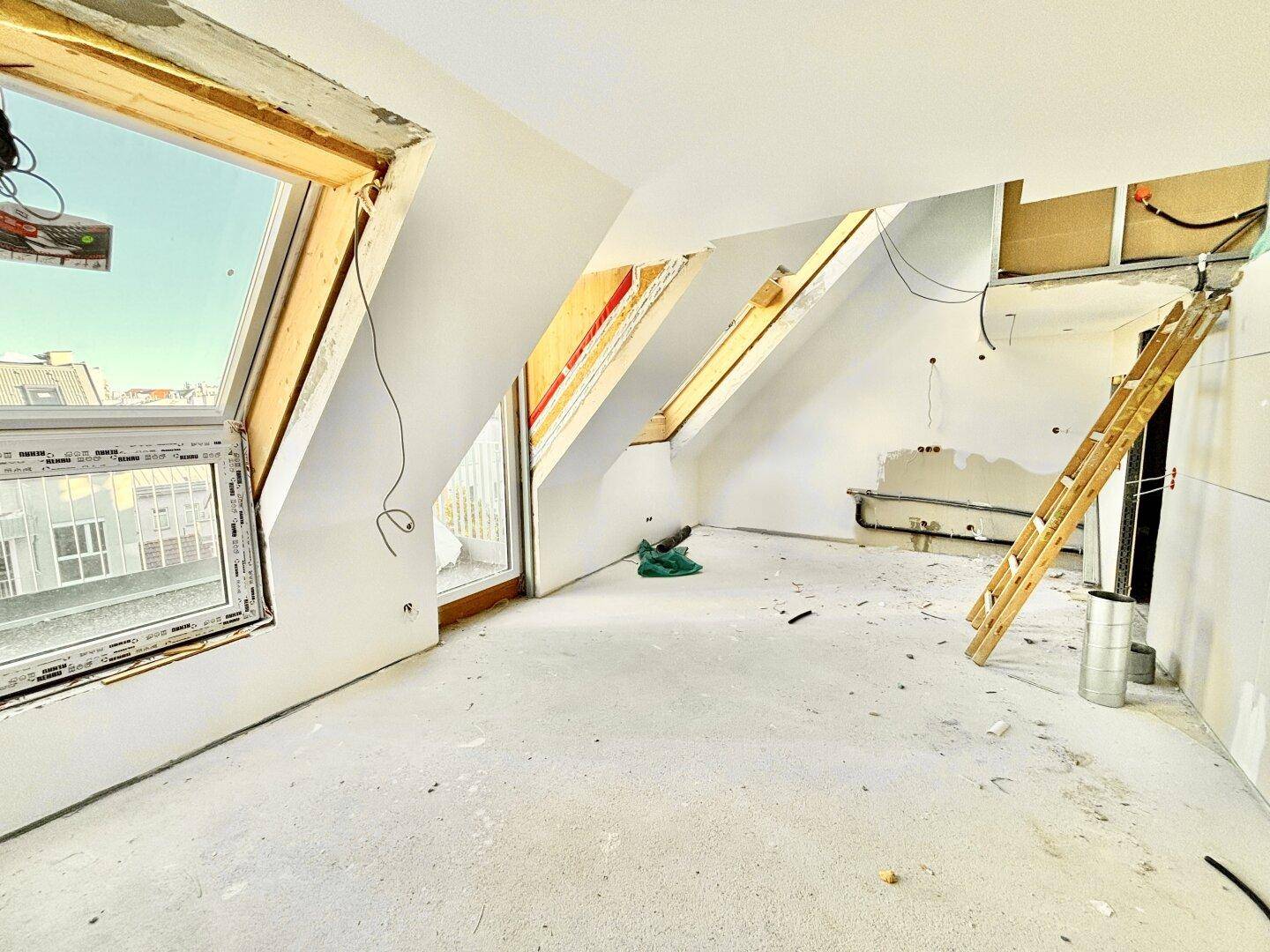Unfertiger Innenraum mit großen Dachfenstern und sichtbaren Bauarbeiten, bereit für den Ausbau.
