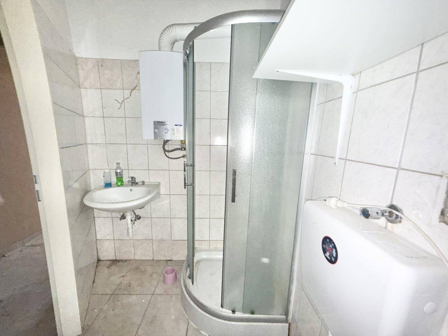 Veraltetes Badezimmer mit Duschkabine und Waschbecken, das auf eine Modernisierung wartet.