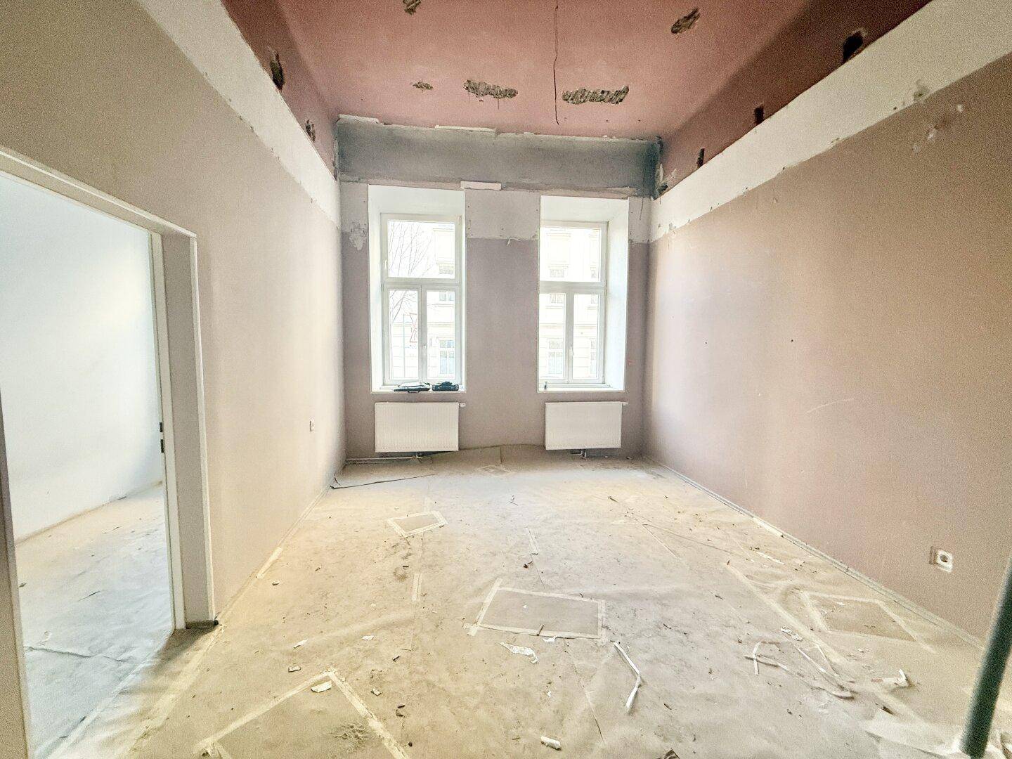 Großer Raum in Renovierung mit hohen Fenstern und vorbereiteten Wänden.