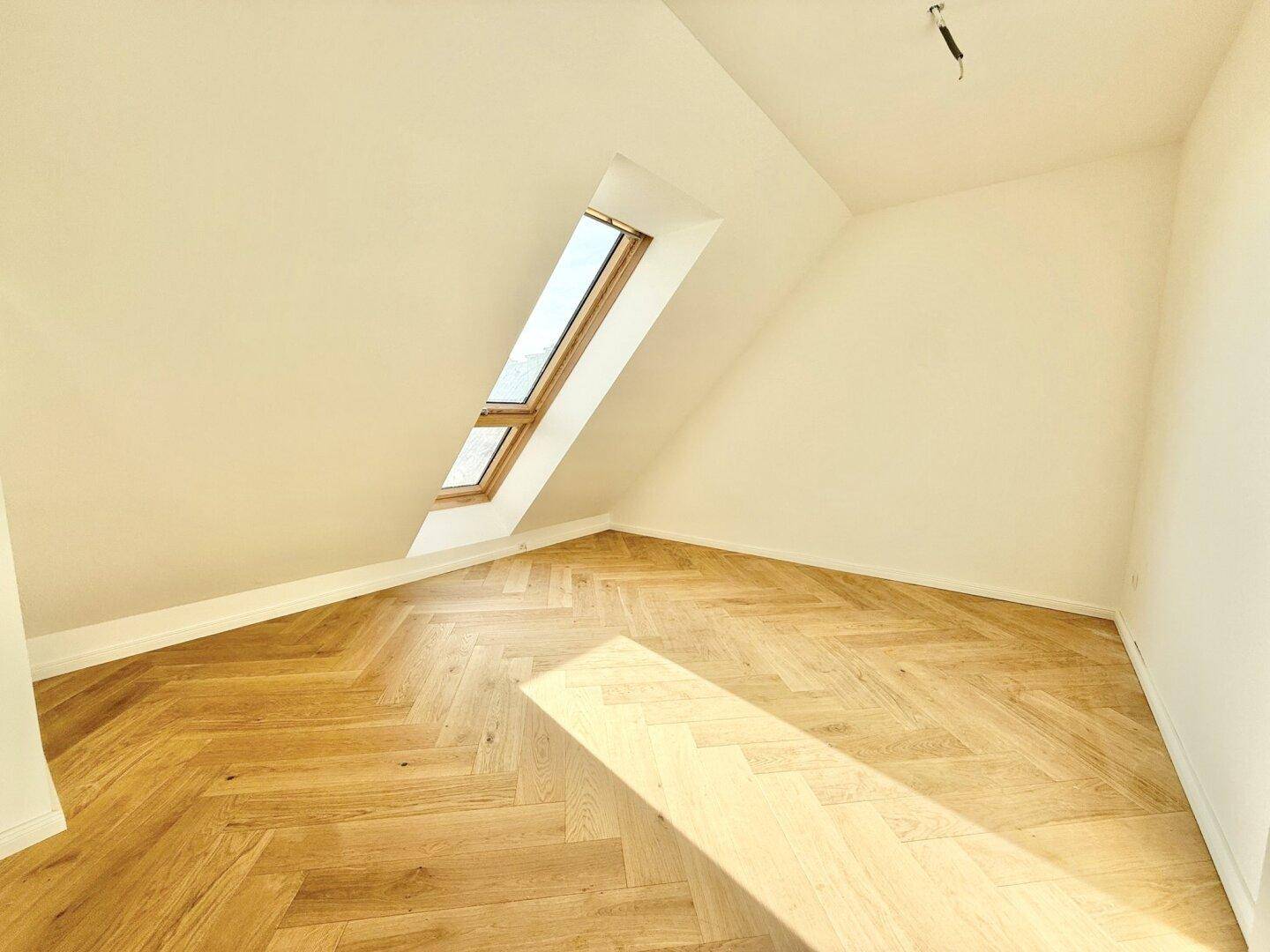 Heller Raum mit Dachschräge und einem einzelnen Dachfenster, ideal als Schlaf- oder Arbeitszimmer.