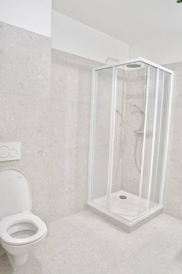 Modernes Badezimmer mit Duschkabine und wandhängendem WC, hell gefliest und funktional gestaltet.