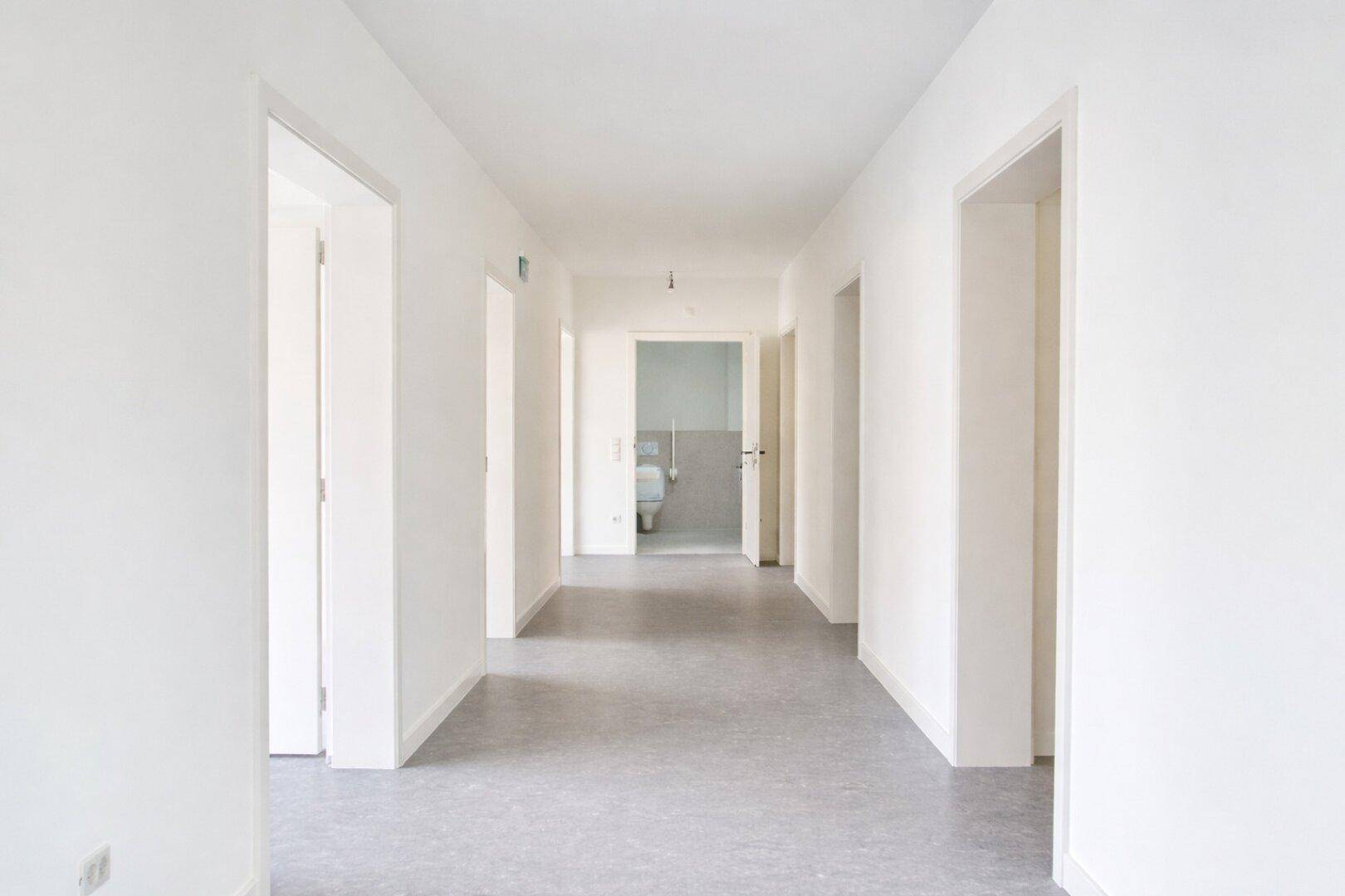 Heller Flur mit mehreren Türen, der zu verschiedenen Räumen führt, mit Blick auf ein Badezimmer am Ende.