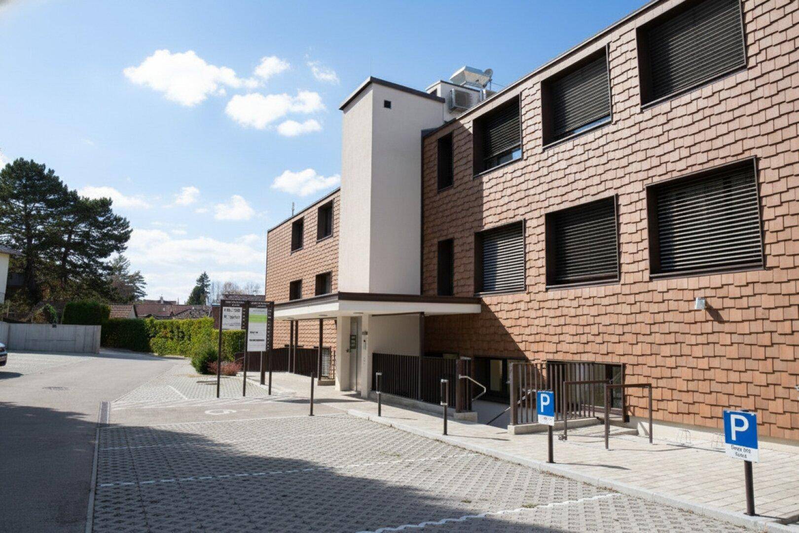 Modernes Gebäude mit markanter Fassade und großzügigen Außenparkplätzen, umgeben von Grünflächen.