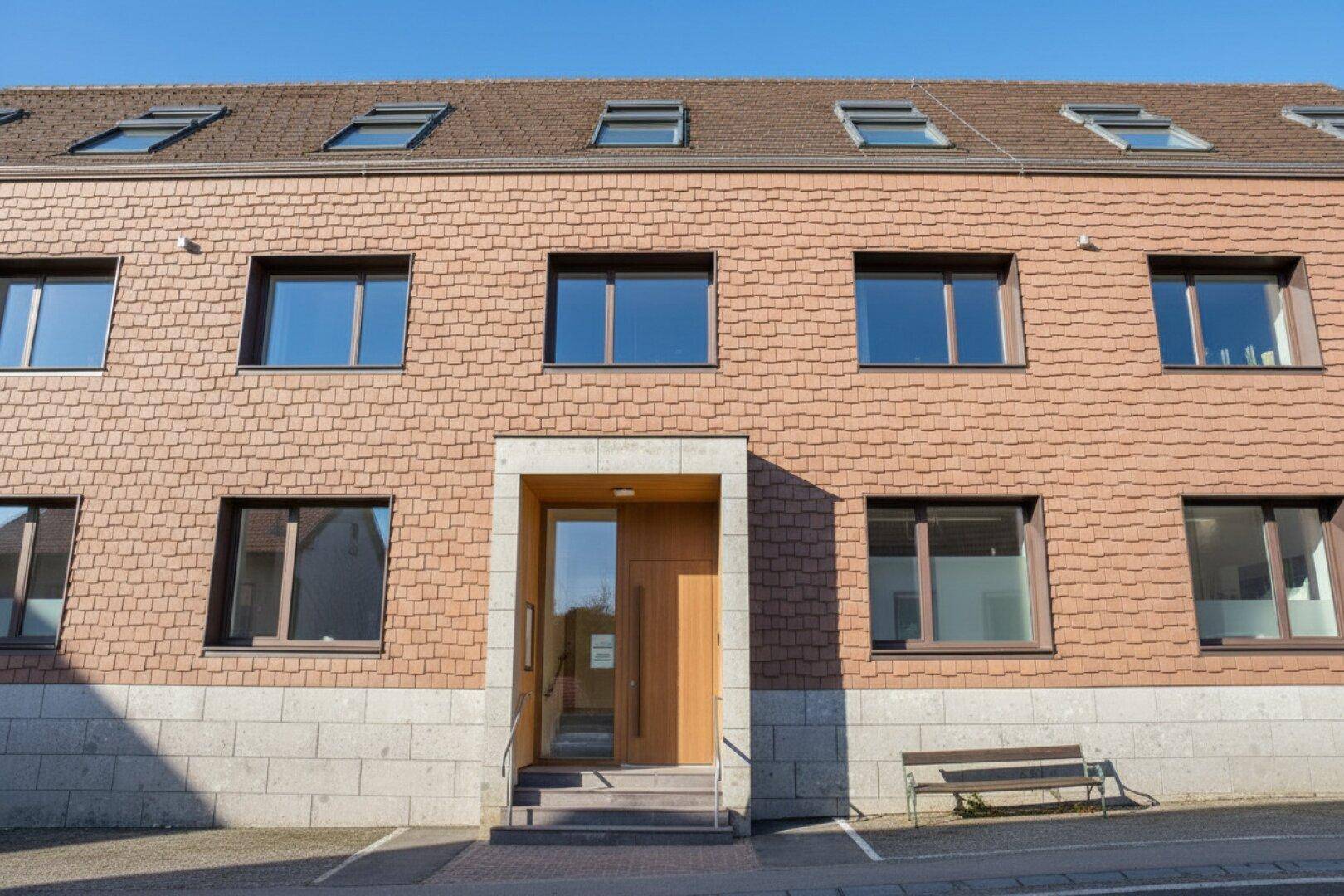 Vorderansicht eines modernen Gebäudes mit markanter Holzschindelfassade und großem Eingangsbereich.