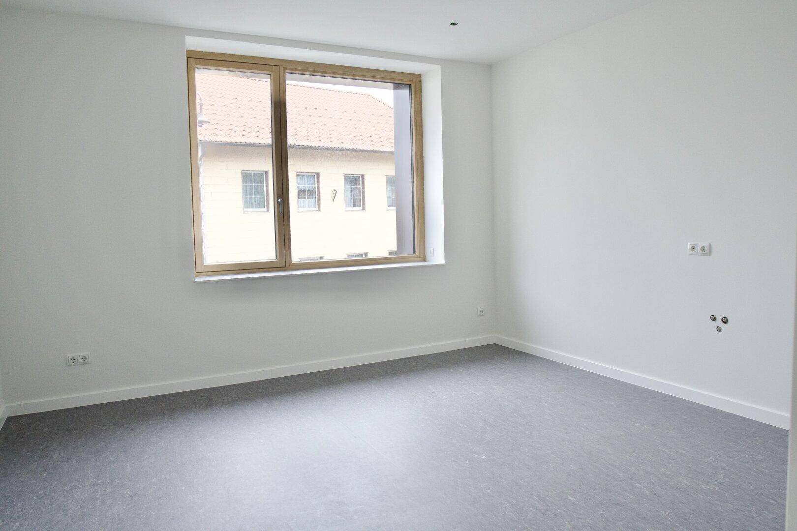 Leerer, heller Raum mit großem Fenster und Blick auf die umliegenden Gebäude, bereit für individuelle Gestaltung.