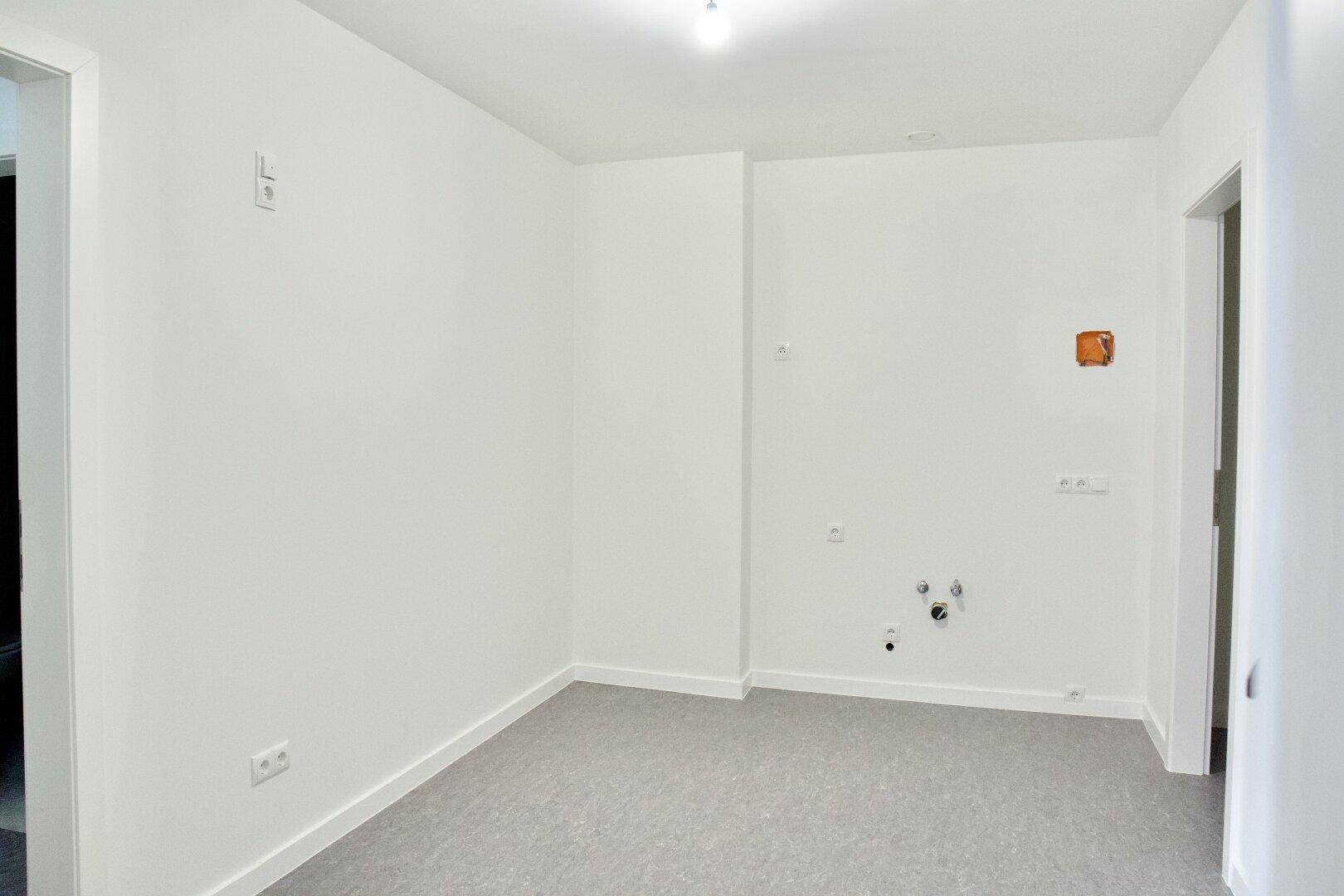 Leerer Raum mit sichtbaren Sanitäranschlüssen und Steckdosen, ideal für die Einrichtung einer Küche oder eines Badezimmers.