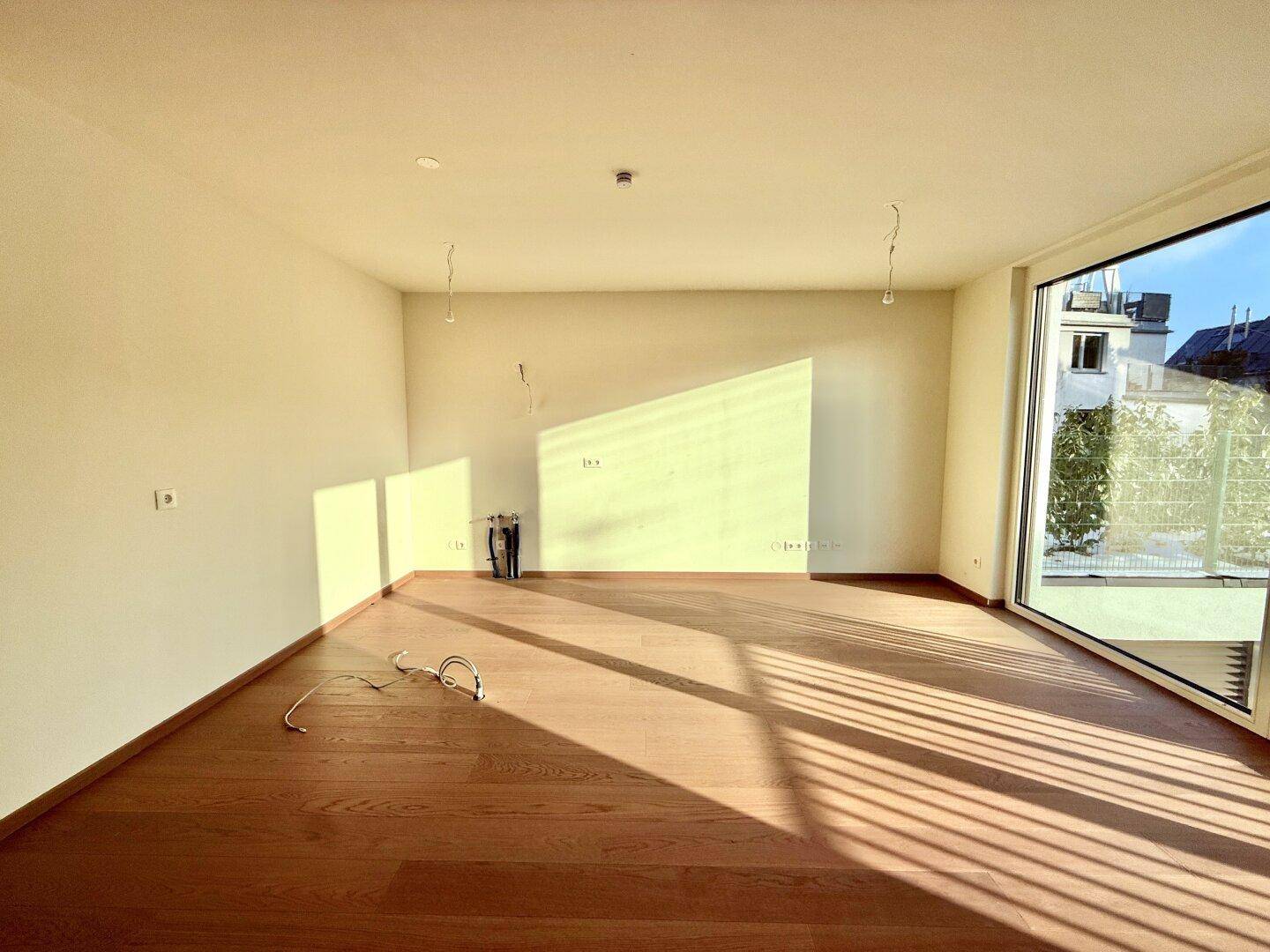 Geräumiger, heller Raum mit Holzboden und einem großen Eckfenster, das viel Licht hereinlässt.