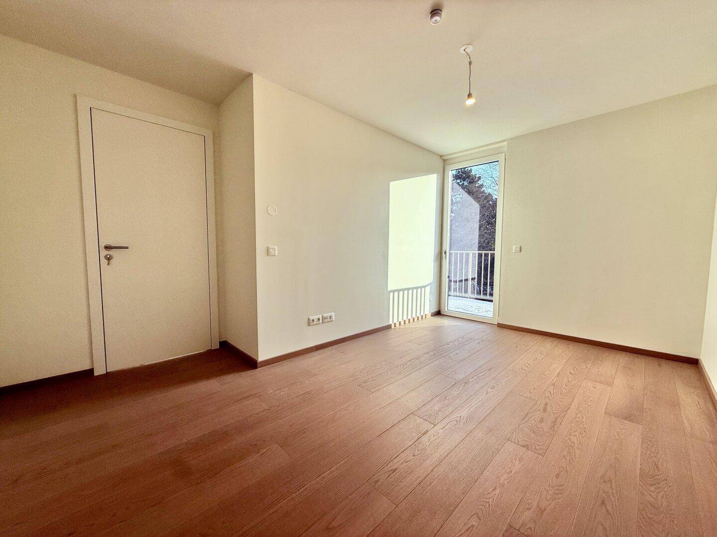 Leeres Schlafzimmer mit Holzboden und Zugang zu einem kleinen Balkon, hell und geräumig.