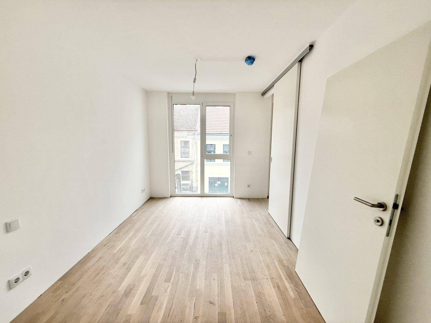 Unmöbliertes Schlafzimmer mit Parkettboden und großem Fenster, bereit zur individuellen Gestaltung.