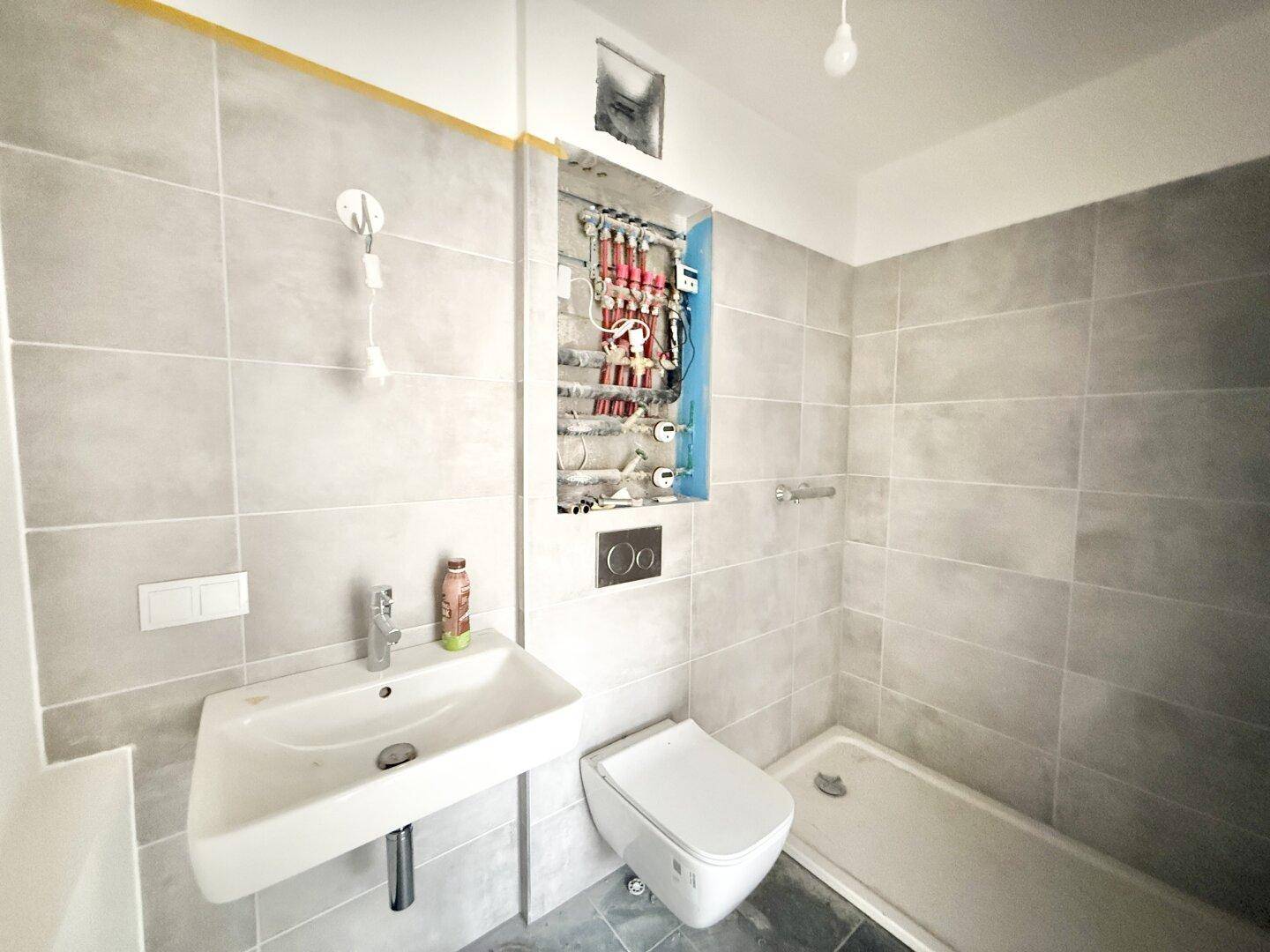Badezimmer im Bau mit Fliesen, Waschbecken, Wand-WC und kleiner Badewanne.