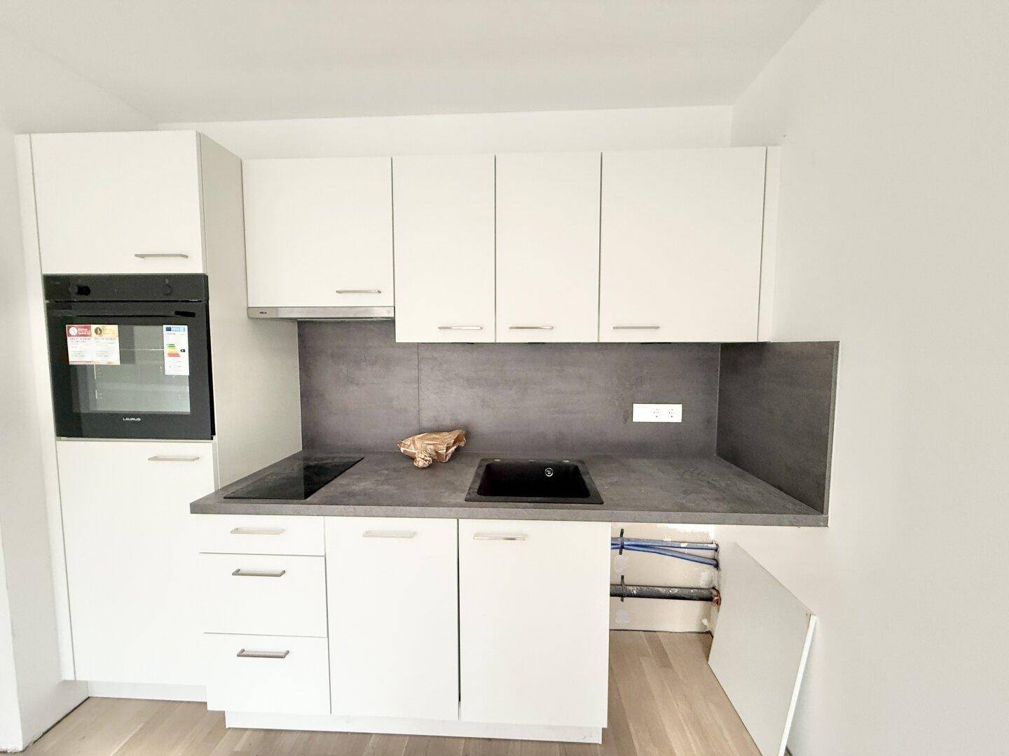 Kompakte, moderne Einbauküche mit weißen Fronten, integriertem Backofen und Induktionskochfeld.