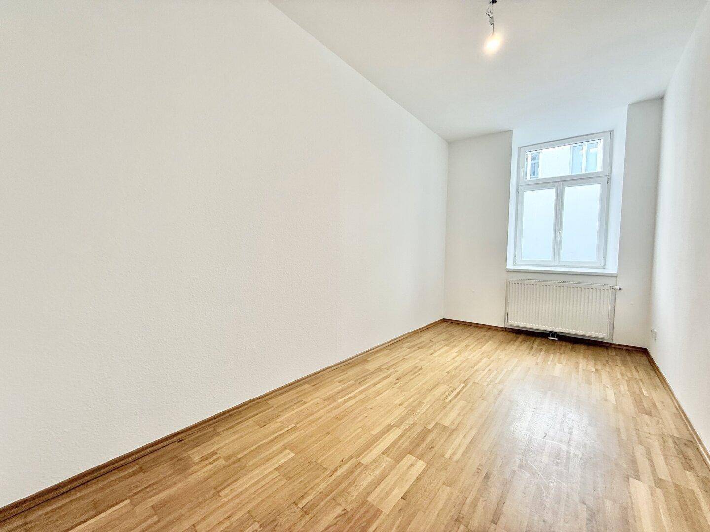 Leerer Raum mit hellem Holzboden und einem Fenster, bereit zur individuellen Gestaltung.