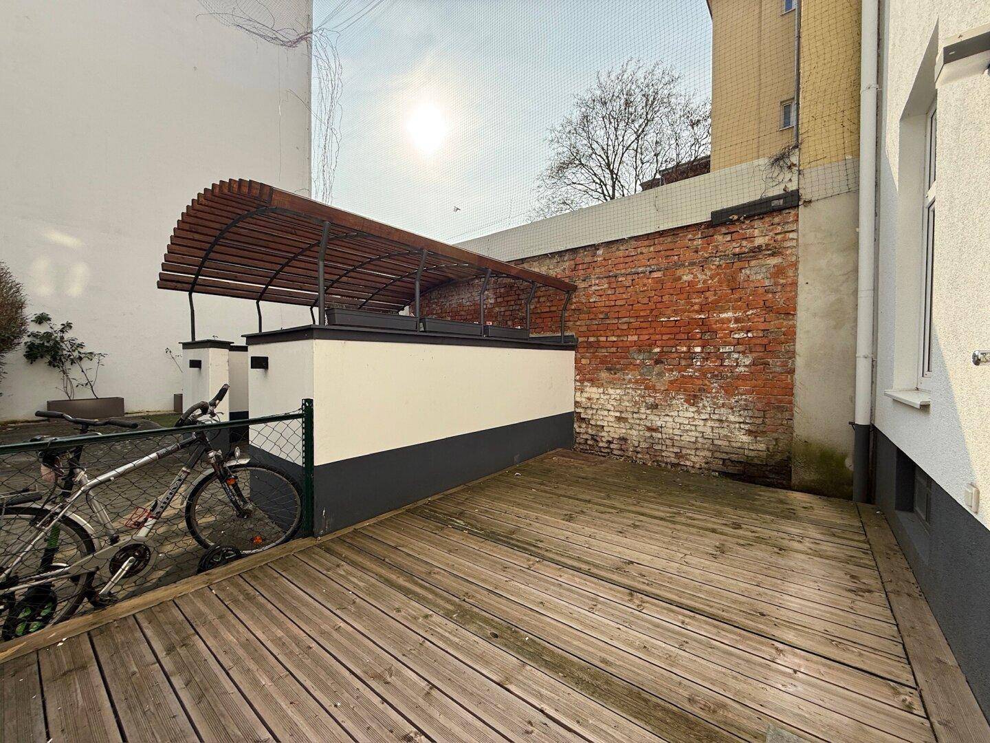 Außenbereich mit Holzdeck und Fahrradstellplatz, umgeben von einer Backsteinmauer.