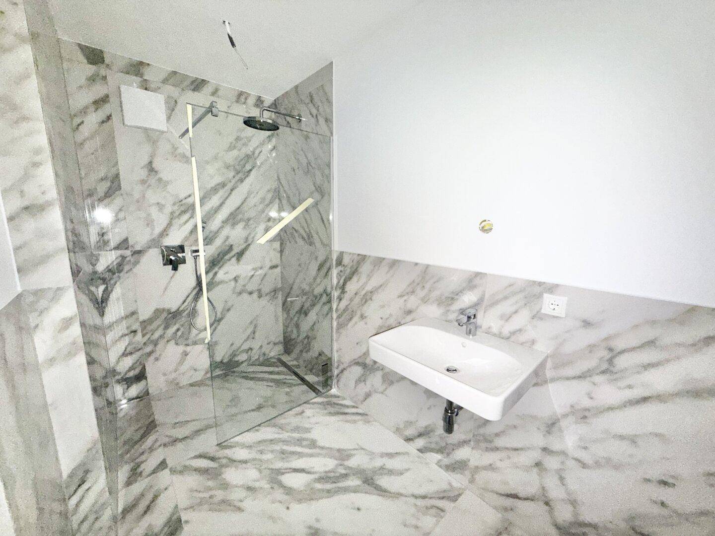 Modernes Badezimmer mit Marmoroptik-Fliesen, großer begehbarer Dusche und Einzelwaschbecken.
