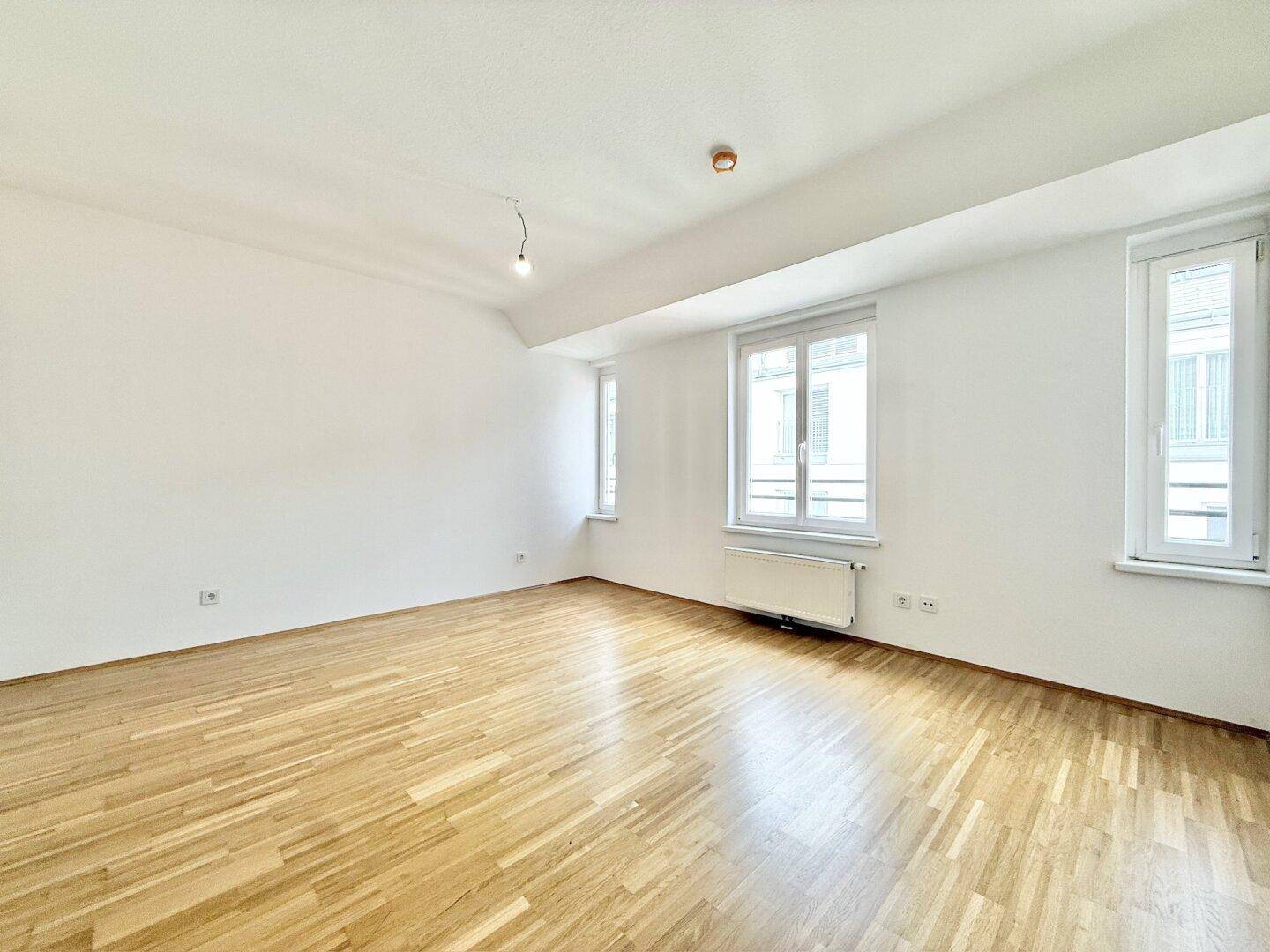 Leerer Raum mit hellem Parkettboden und großen Fenstern, ideal für Schlaf- oder Wohnzimmer.