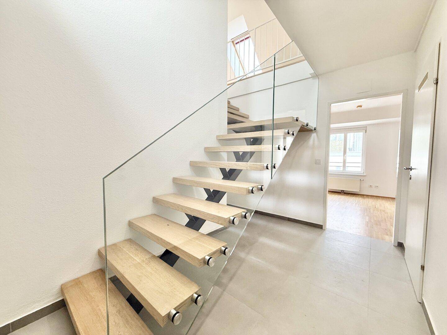 Moderne Treppe mit Holzstufen und Glasgeländer, die zu den oberen Etagen führt.