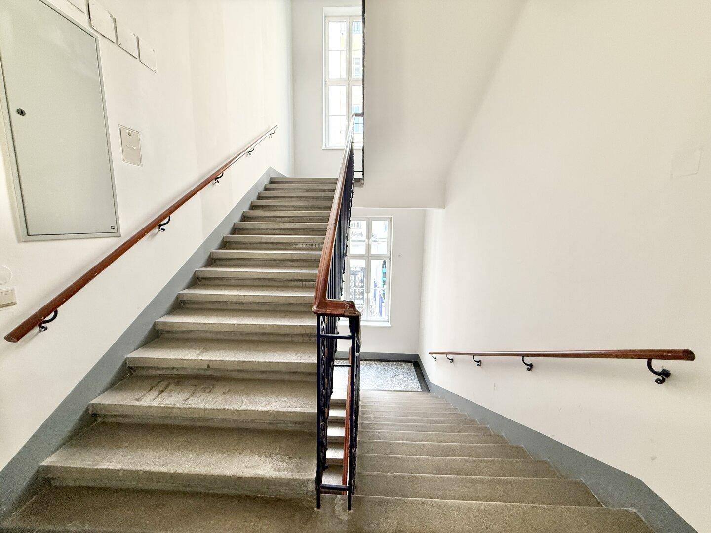 Geräumiges Treppenhaus mit Steinstufen, Holzhandläufen und Fenstern für Tageslicht.