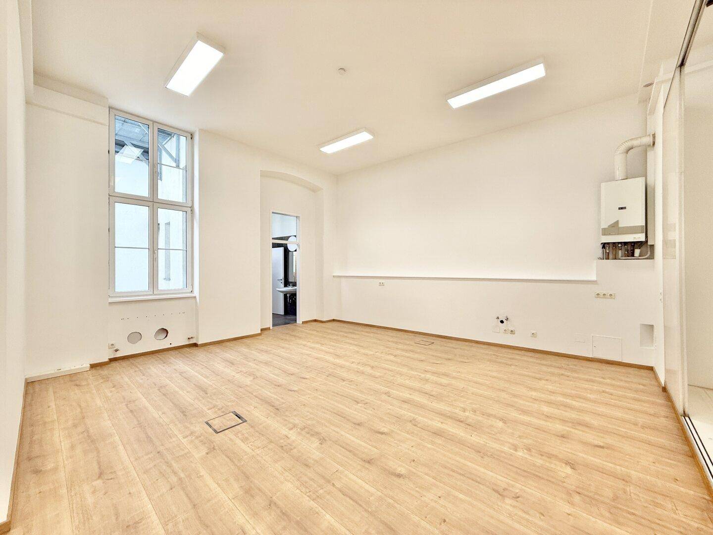 Leerer Büroraum mit Gastherme an der Wand und Zugang zu einem Nebenraum.