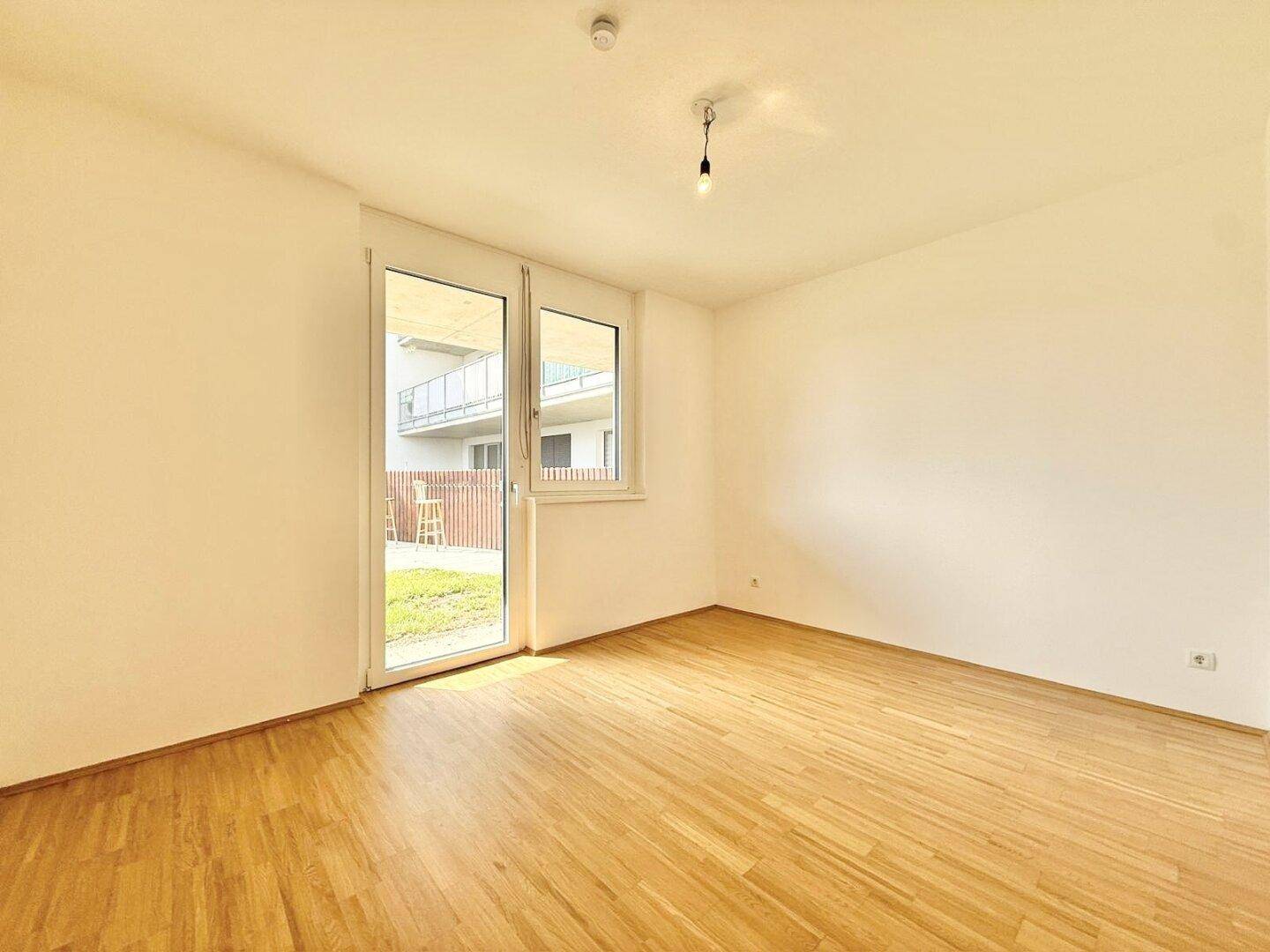 Heller, leerer Raum mit Holzboden und großen Fenstern, bietet viel Tageslicht und Zugang nach draußen.