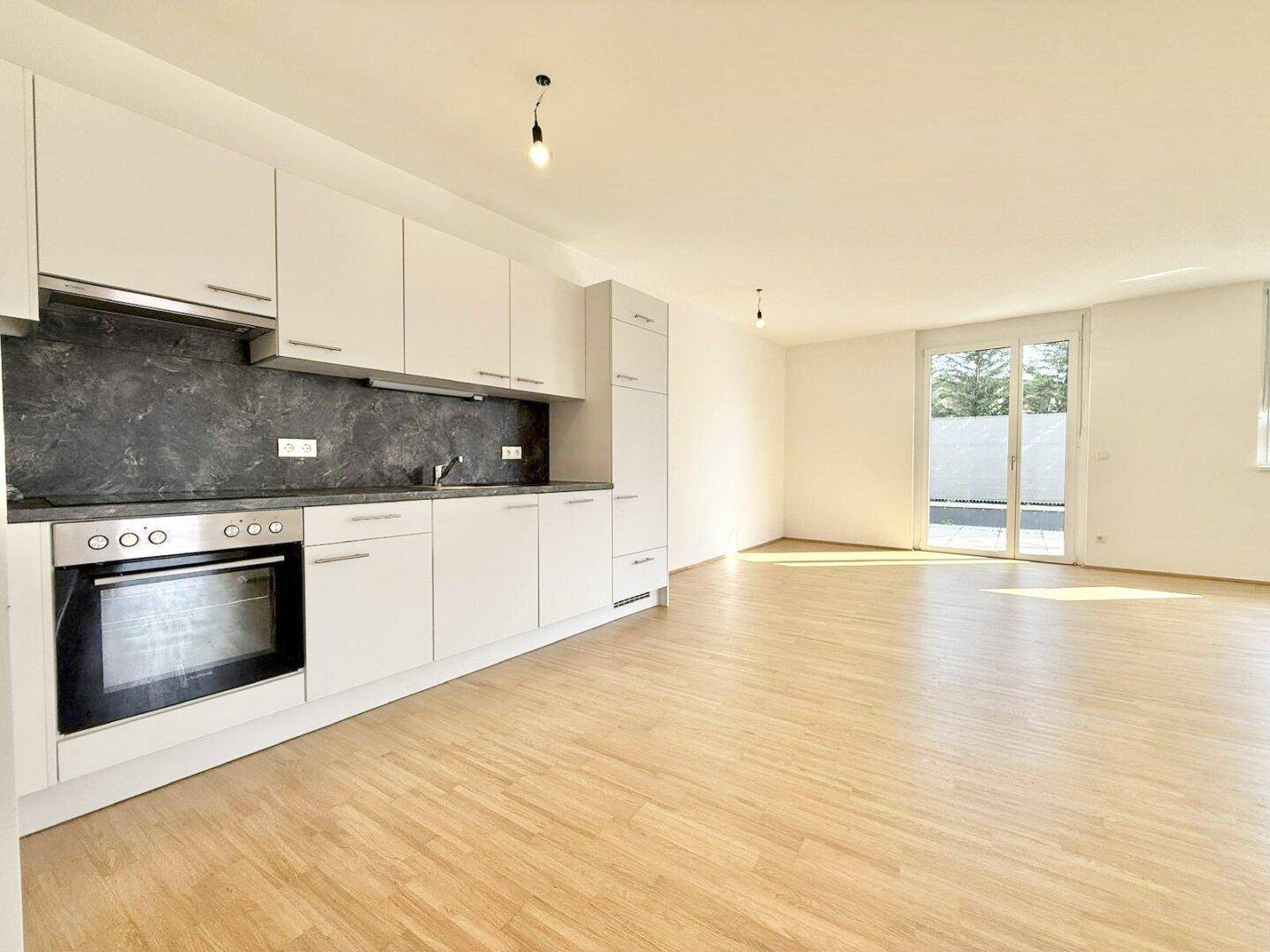 Moderne Einbauküche mit weißen Schränken, dunkler Arbeitsplatte und Holzboden, mit Balkonzugang.