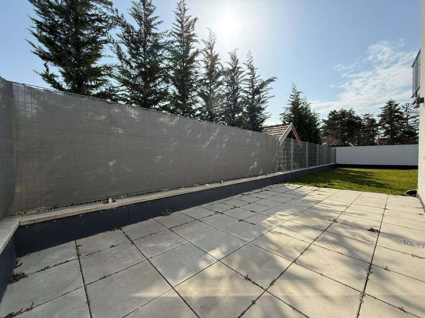 Geräumige gepflasterte Terrasse neben einer Rasenfläche, umgeben von einem Sichtschutzzaun.