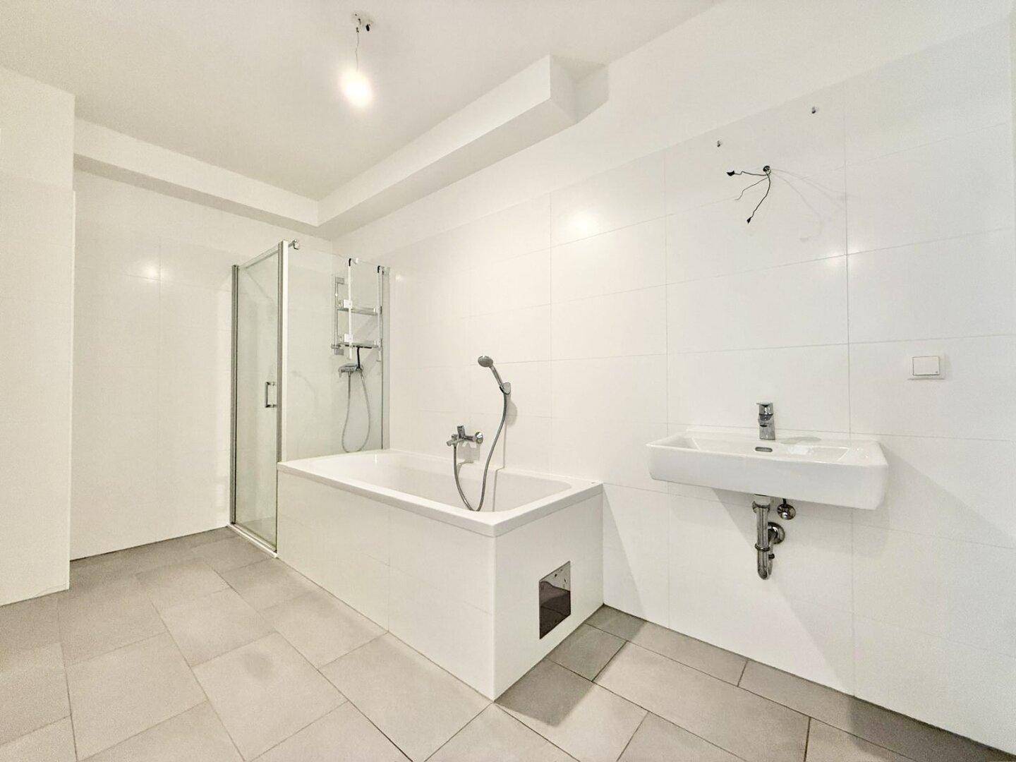 Modernes Badezimmer mit weißen Fliesen, Badewanne mit Duschabtrennung und Waschbecken.