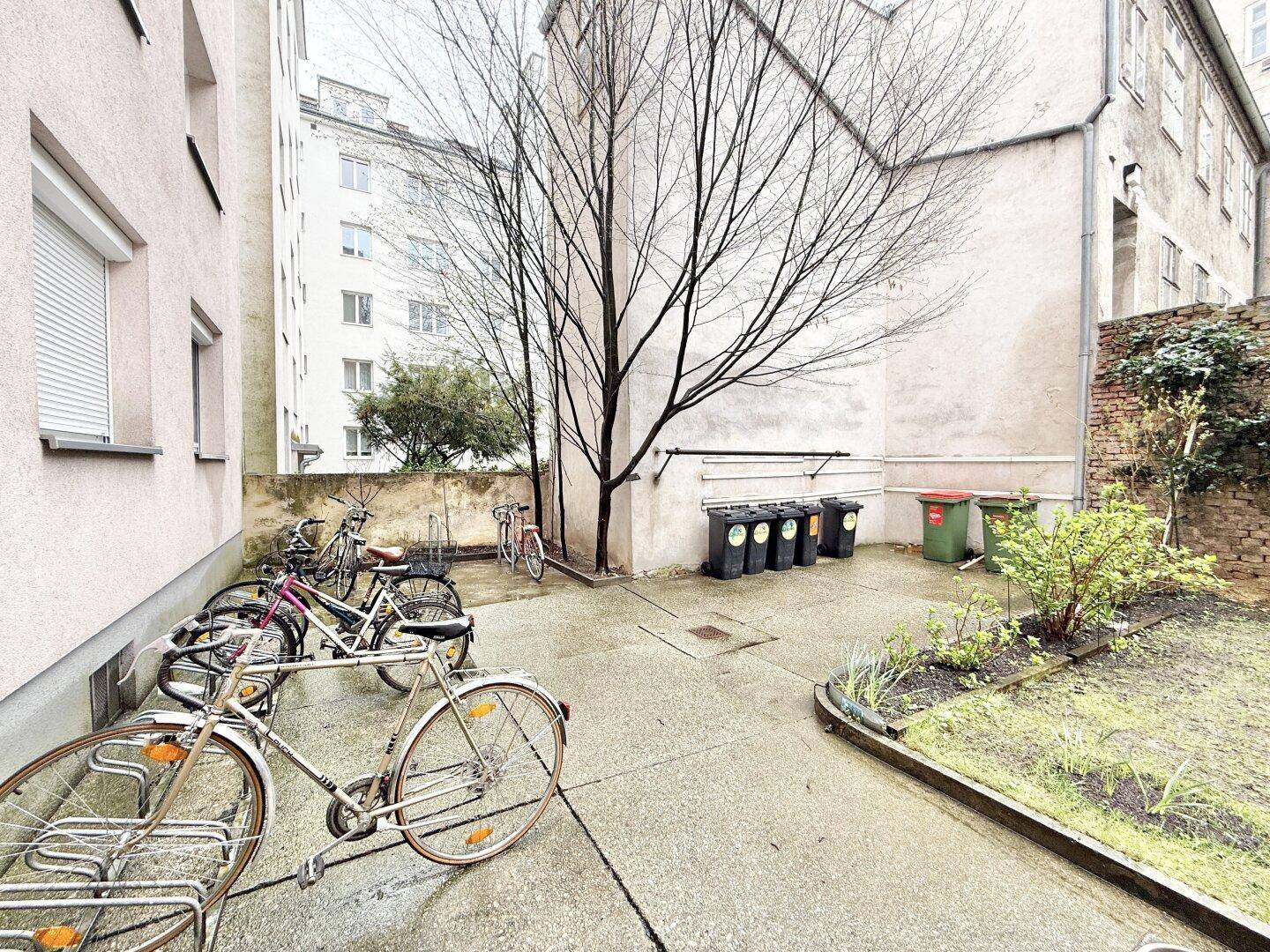 Innenhof mit Fahrradabstellplätzen und Mülltonnen, umgeben von Gebäuden.