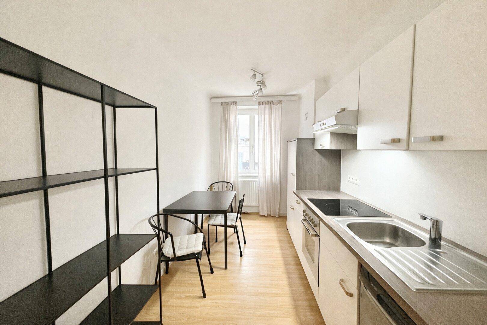 Funktionale Küche mit weißen Schränken, Essbereich und Fenster für Tageslicht.