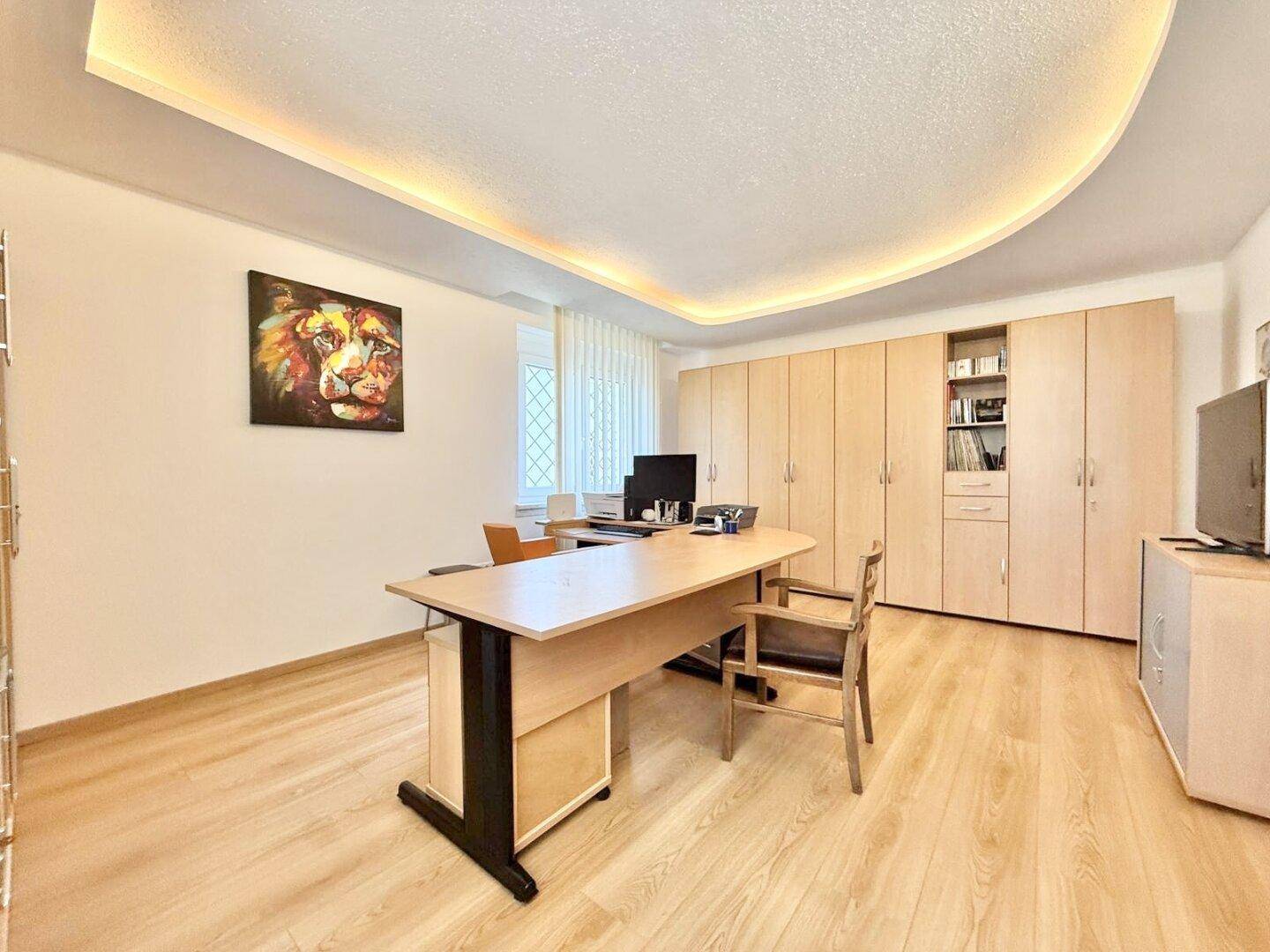 Geräumiges Büro mit Holzschränken, Schreibtisch und indirekter Deckenbeleuchtung.