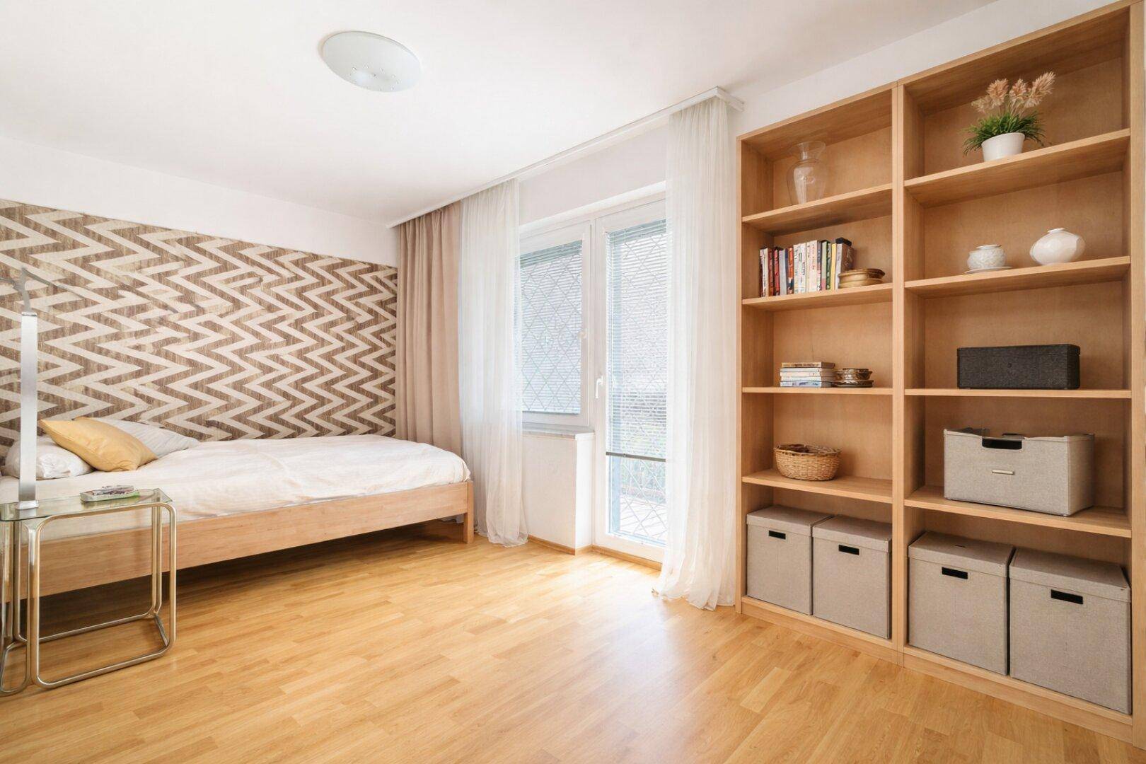 Helles Schlafzimmer mit Einzelbett, Holzregal und dekorativer Wandtapete.