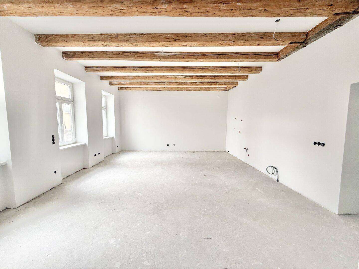 Geräumiger, unmöblierter Raum mit sichtbaren Holzbalken und Rohbauzustand, bereit für Ausbau.