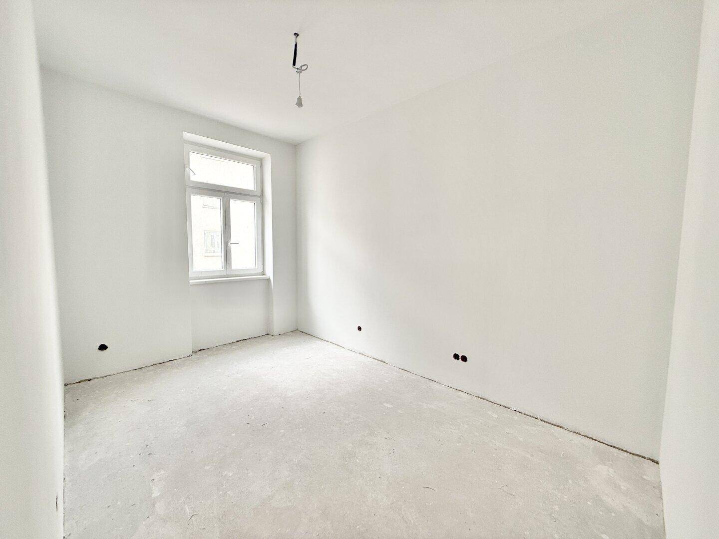 Leerer Raum mit einem Fenster und weiß gestrichenen Wänden, im Rohbauzustand.