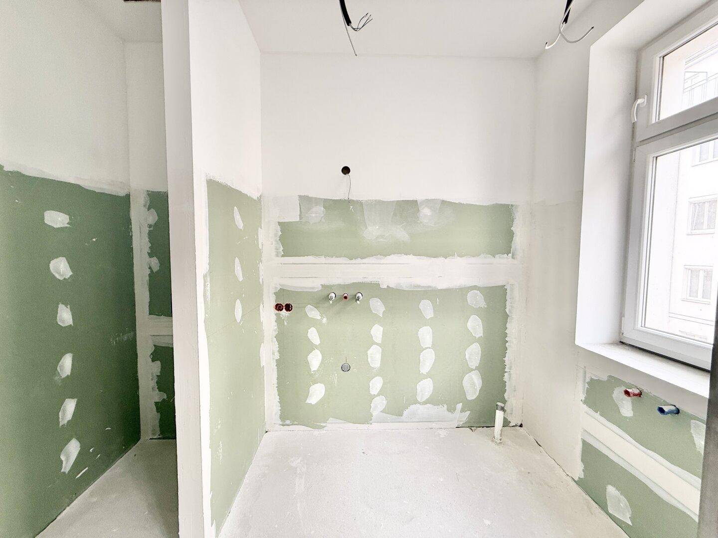 Badezimmer im Rohbauzustand mit vorbereiteten Installationen und Fenster, bereit für den Ausbau.