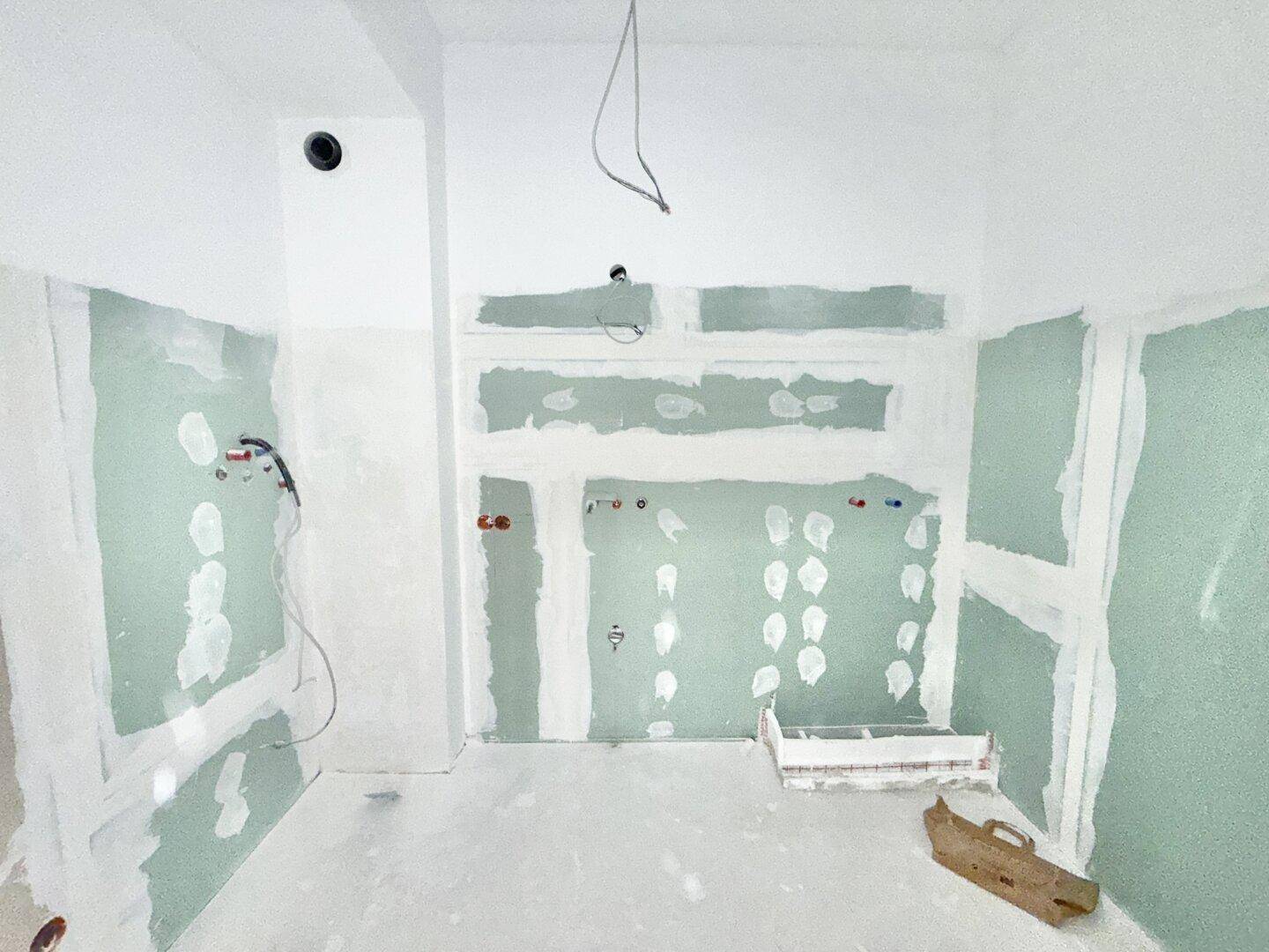 Badezimmer im Rohbau mit sichtbaren Installationen und grünen Gipskartonplatten, bereit für den Ausbau.