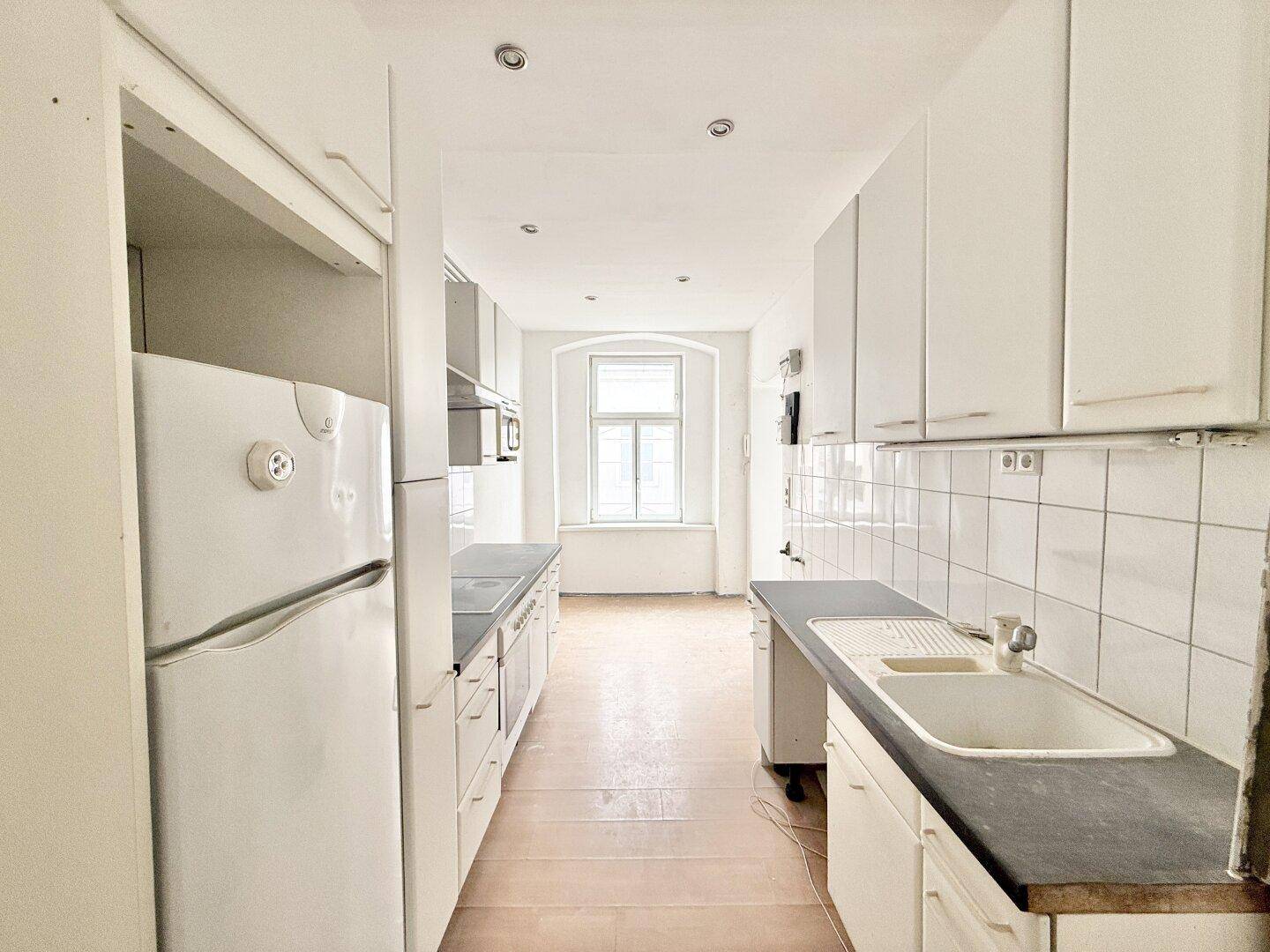 Helle Küche mit weißen Schränken, Spüle und Kühlschrank, bereit für eine Renovierung.