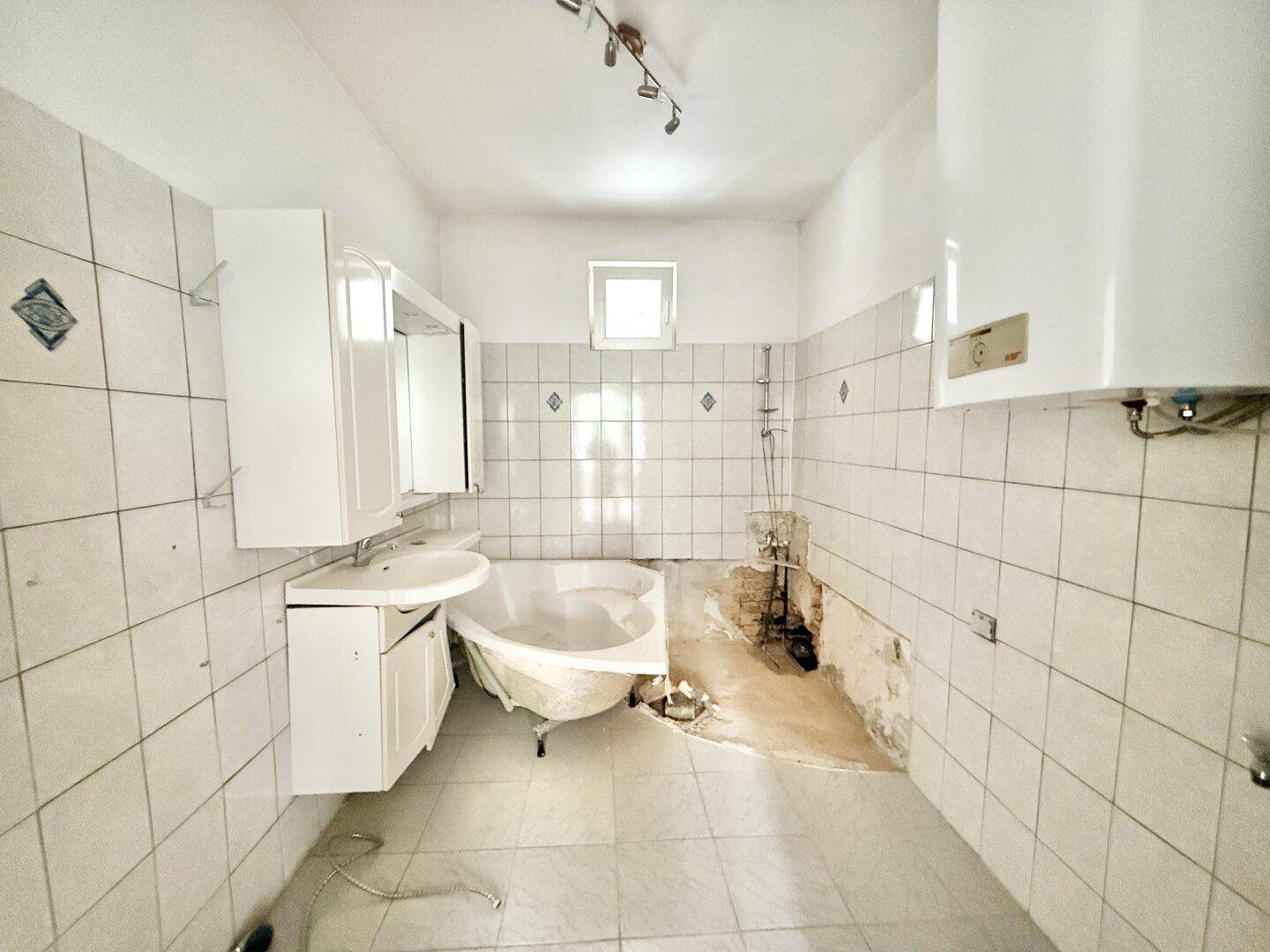 Badezimmer in sanierungsbedürftigem Zustand mit Badewanne, Waschbecken und Fenster.