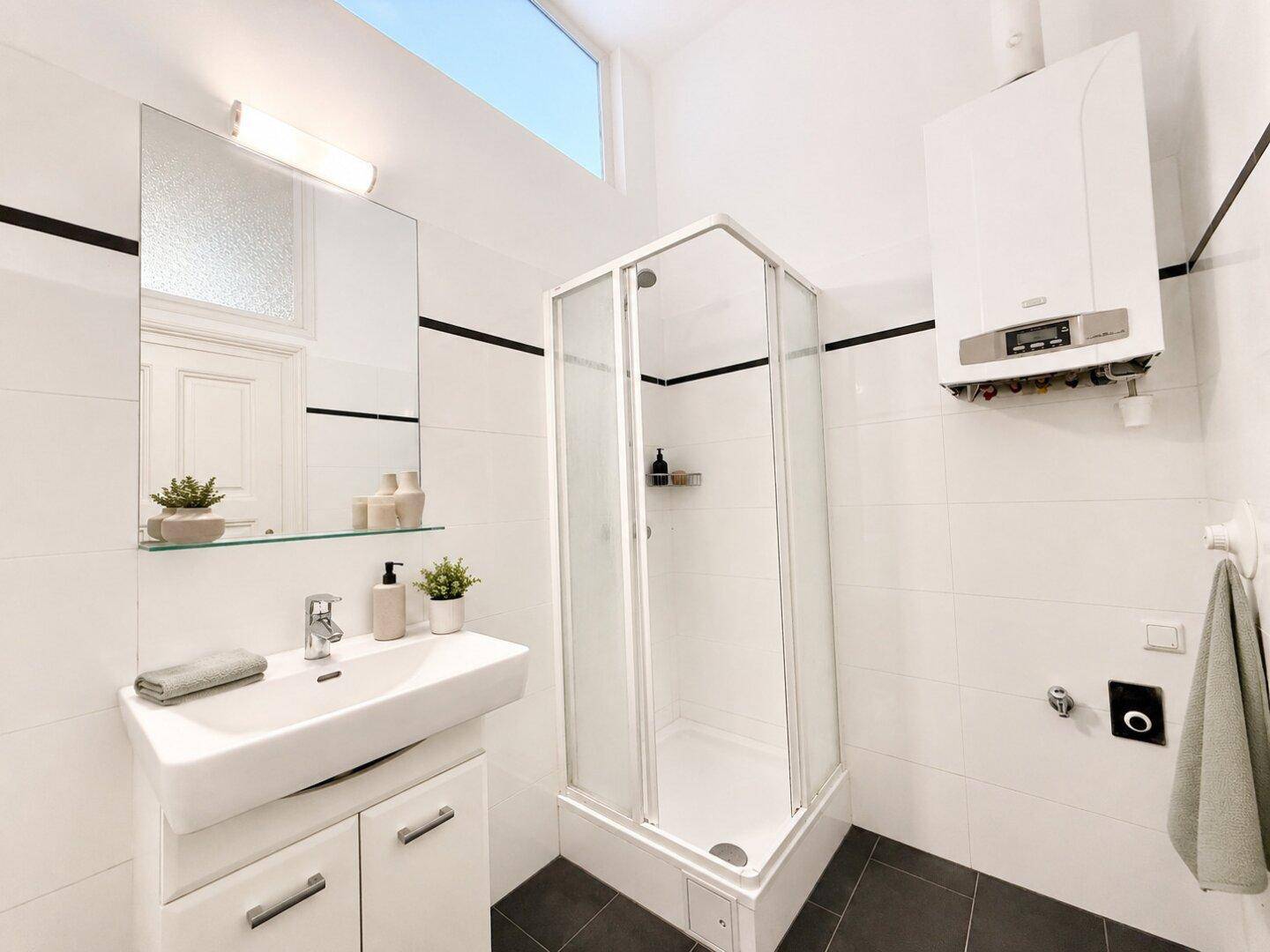 Modernes Badezimmer mit Duschkabine, Einzelwaschbecken und Gastherme, hell gefliest mit dunklem Boden.