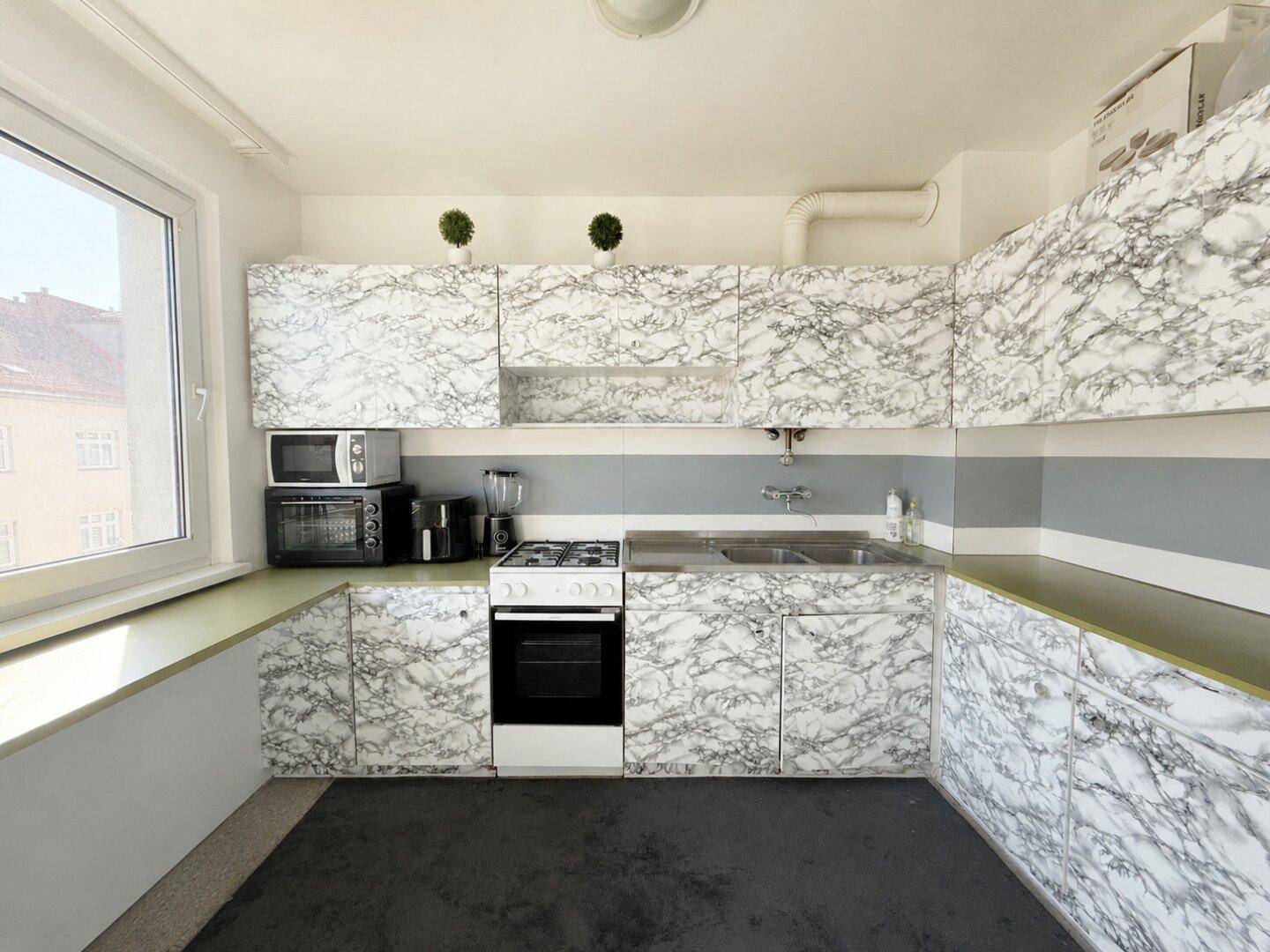 Leere Küche mit älteren Schränken im Marmor-Look, Gasherd und Teppichboden.