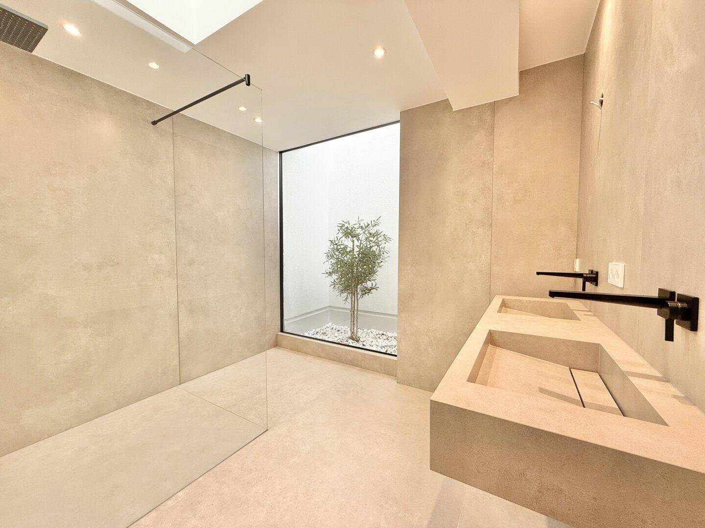 Modernes Badezimmer mit Doppelwaschbecken, begehbarer Dusche und Innenhof mit Bepflanzung.